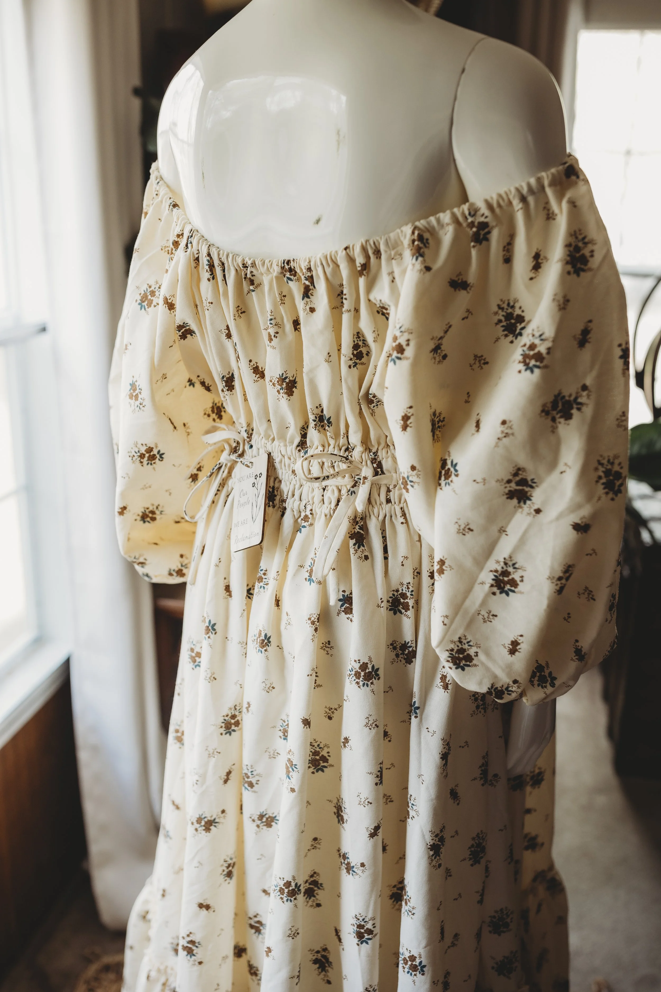 Soft cream floral dress with an elastic waist and sleeves worn up for a modest look, photographed indoors.