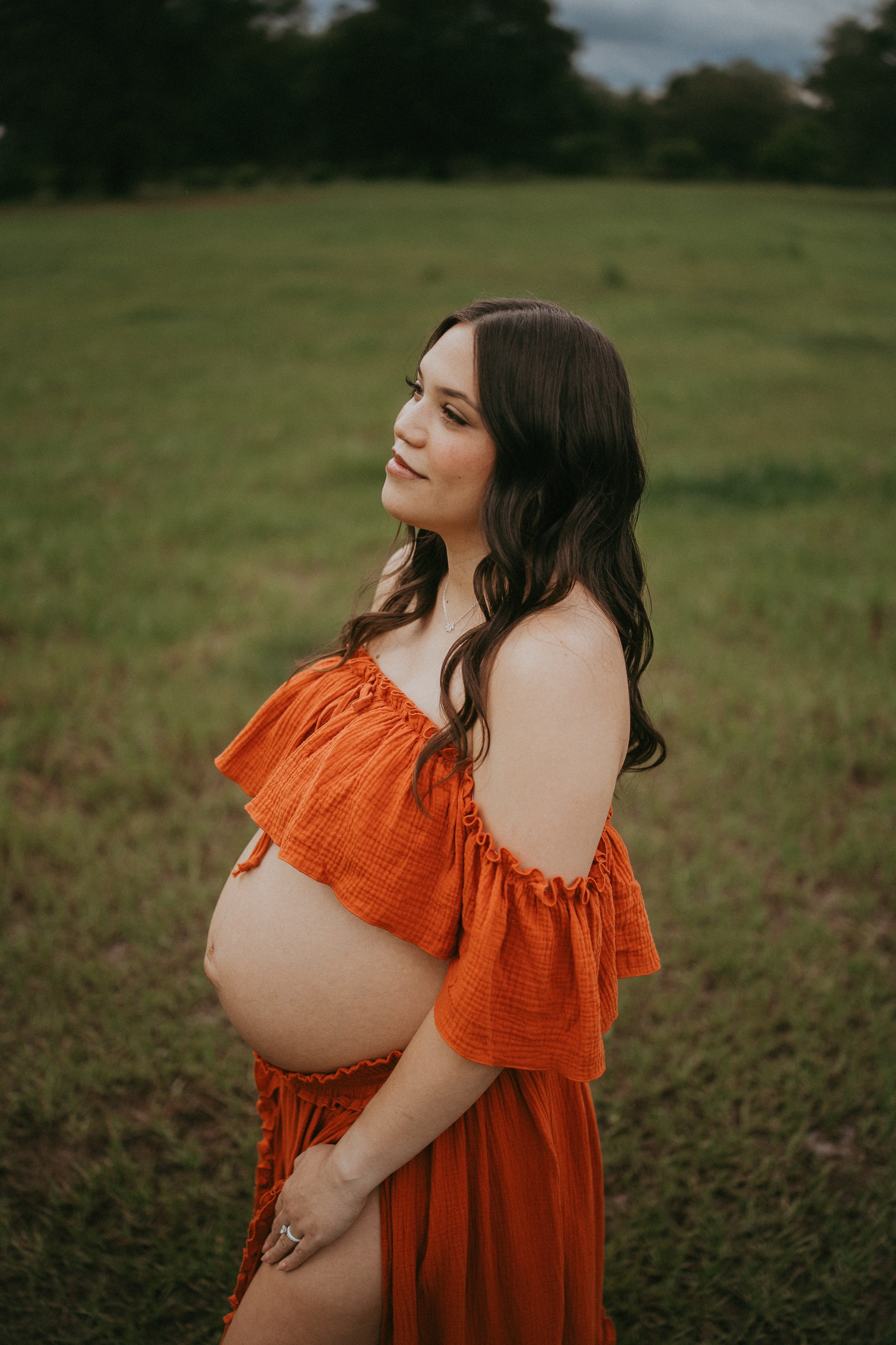 Expectant mother in a flowing rust-colored dress during an outdoor maternity portrait in Hilliard, Florida.