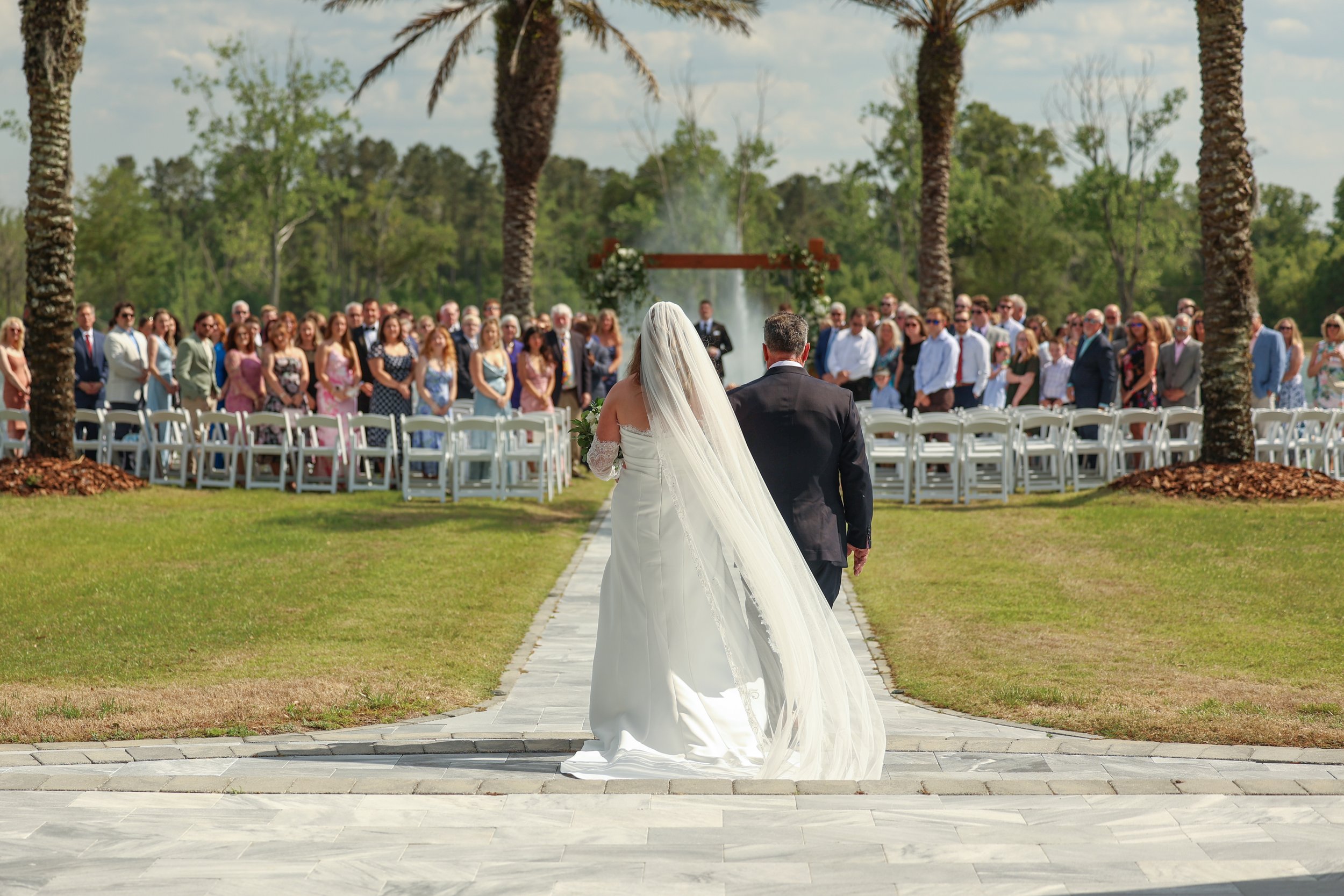Bride walks down the aisle with her father toward an outdoor lakeside ceremony at Cottonwood Ranch in Callahan, Florida.