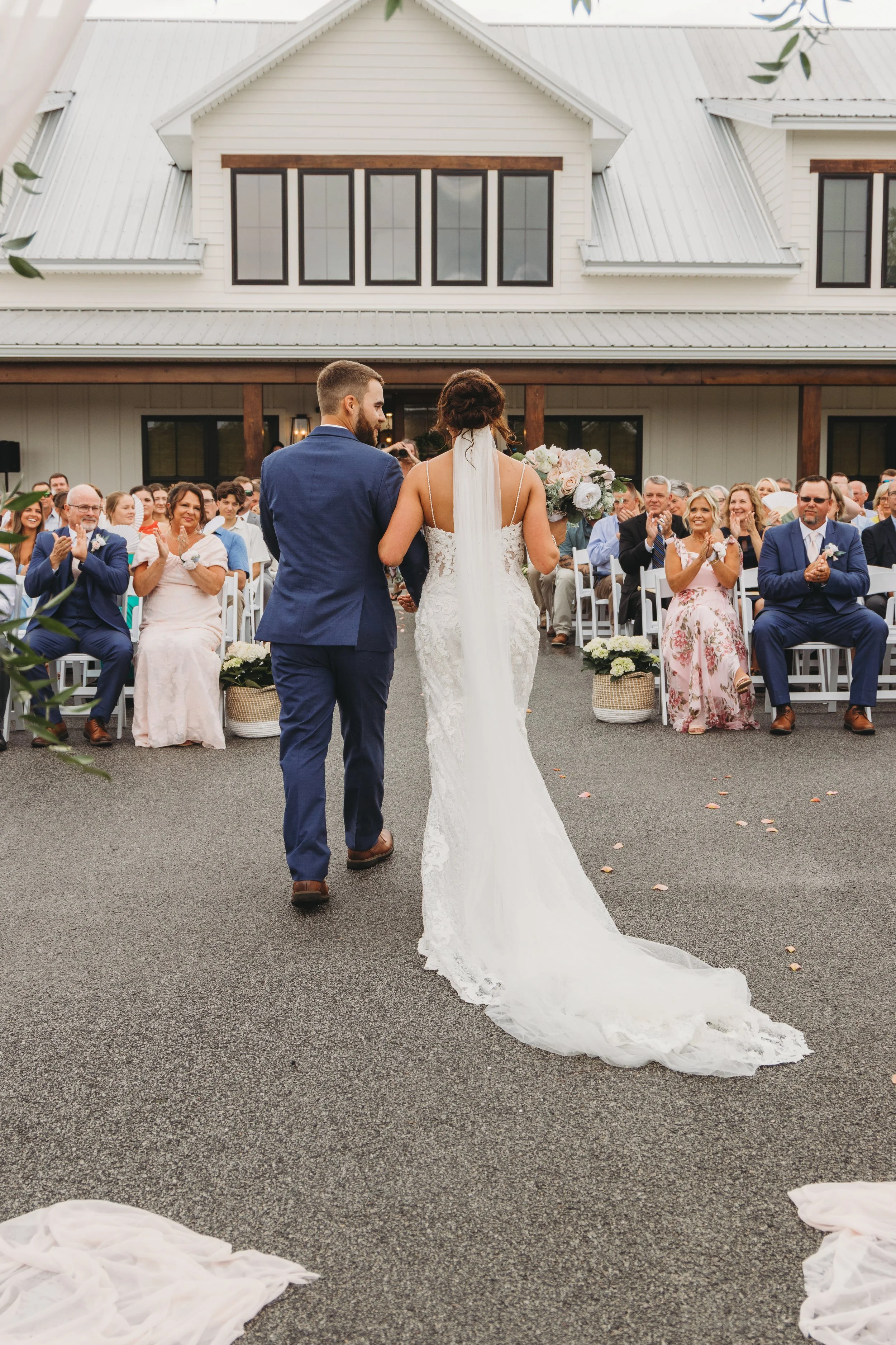 Emma and Dylan walk hand in hand down the aisle as guests applaud after their outdoor wedding ceremony at Red River Estate.