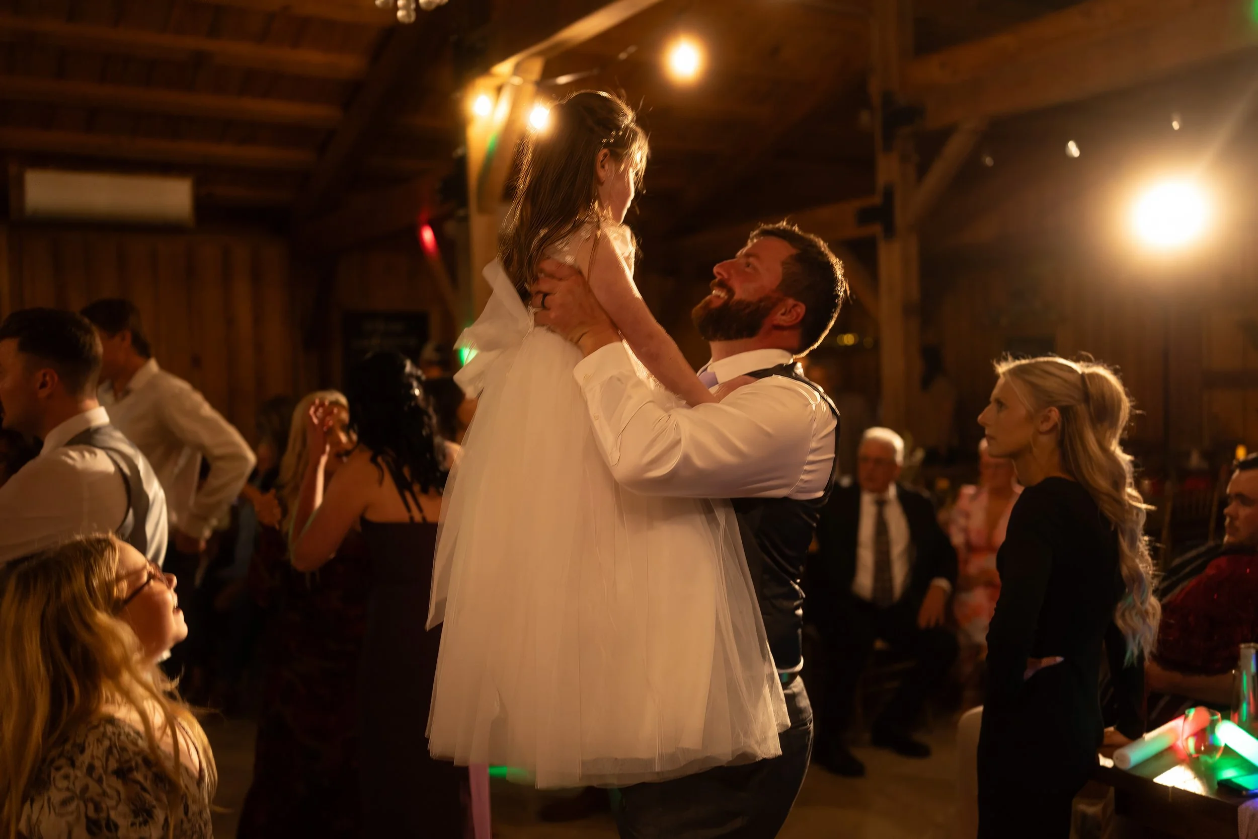 Emotional father-daughter dance as he lifts her beneath warm reception lights.