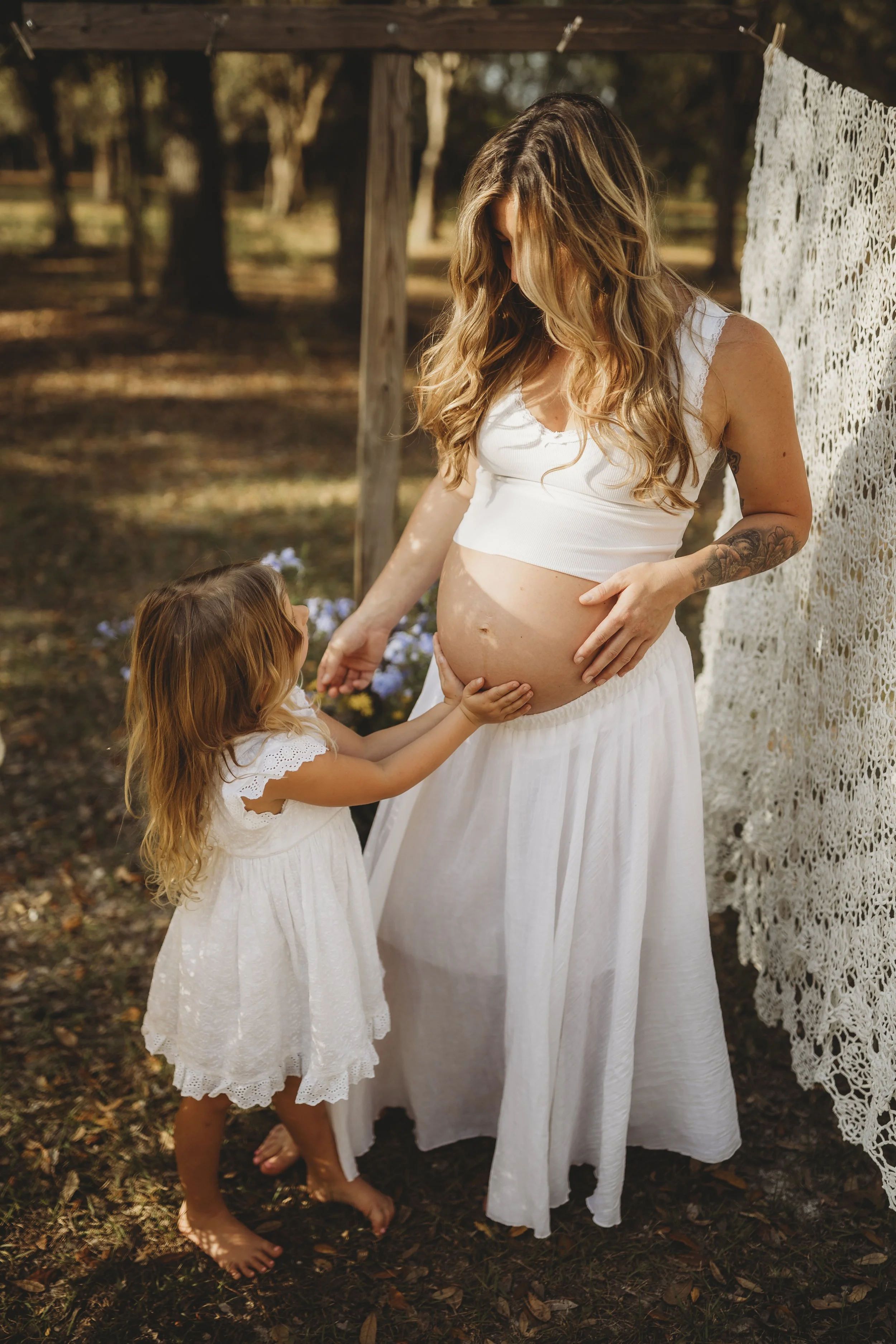A candid moment of motherhood—laughter, touch, and connection—where one child clings close while another is lovingly awaited.