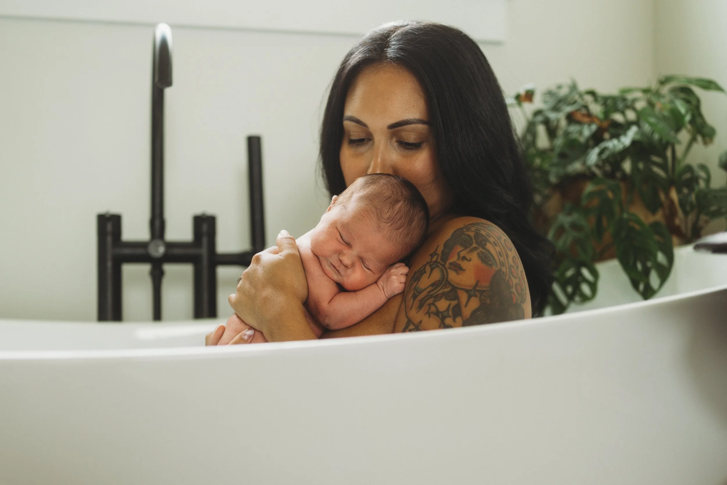 Mother cuddling and kissing her sleeping newborn during a relaxed in-home lifestyle newborn session, capturing a quiet moment of love and connection.