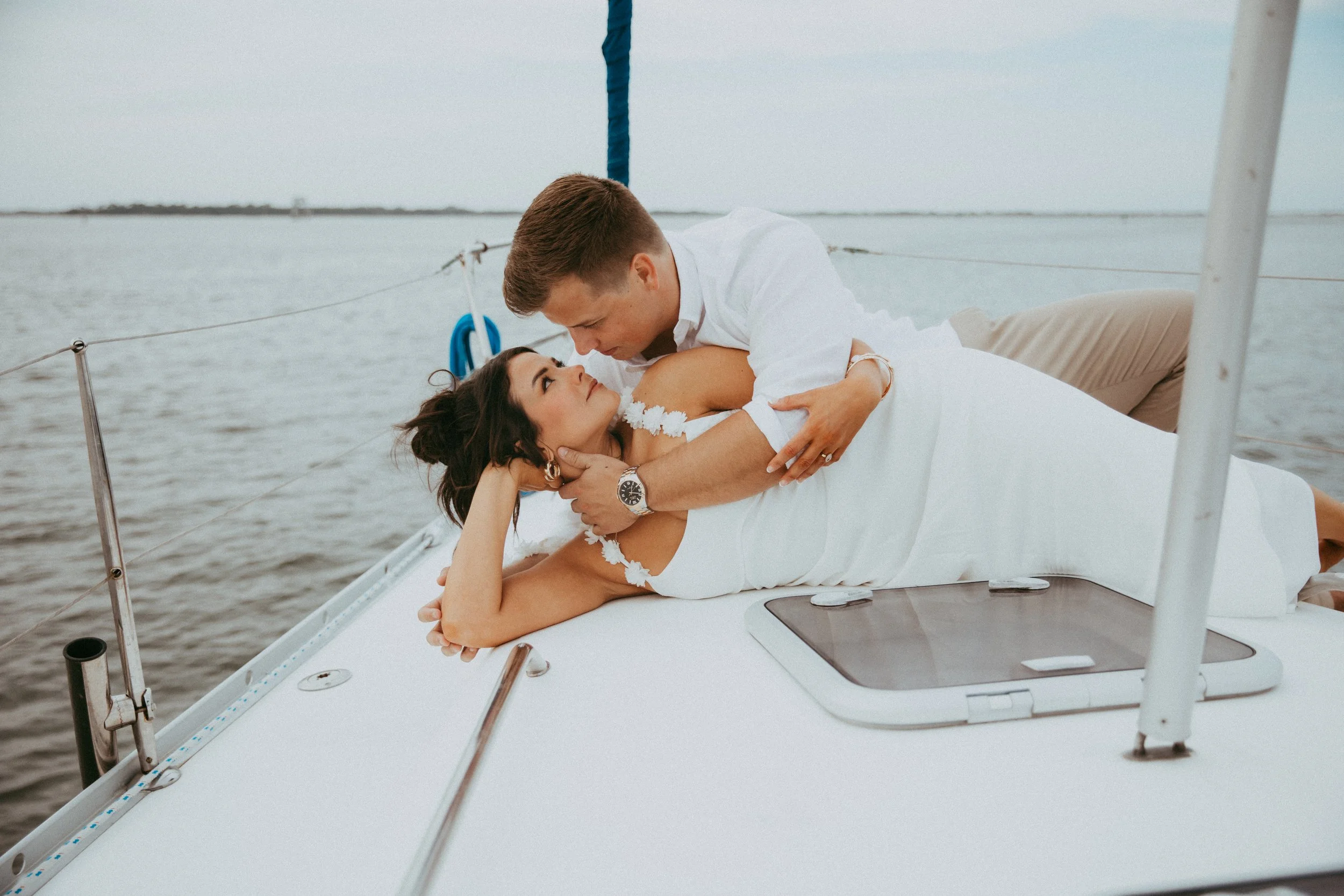 Adam leans over Lyndsey as they laugh together on the sailboat deck