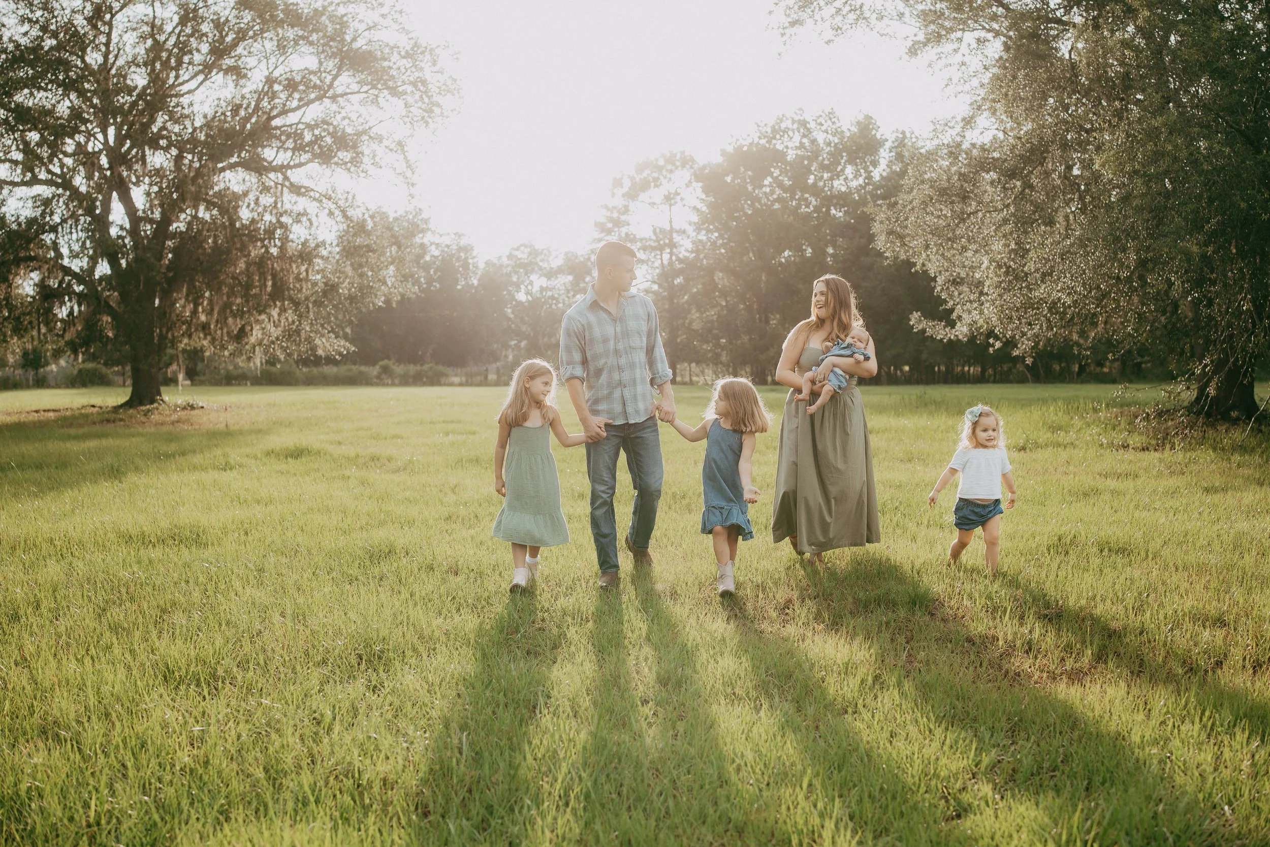 Family of six walking and playing together in a sunlit field during a relaxed outdoor family photography session in Northeast Florida