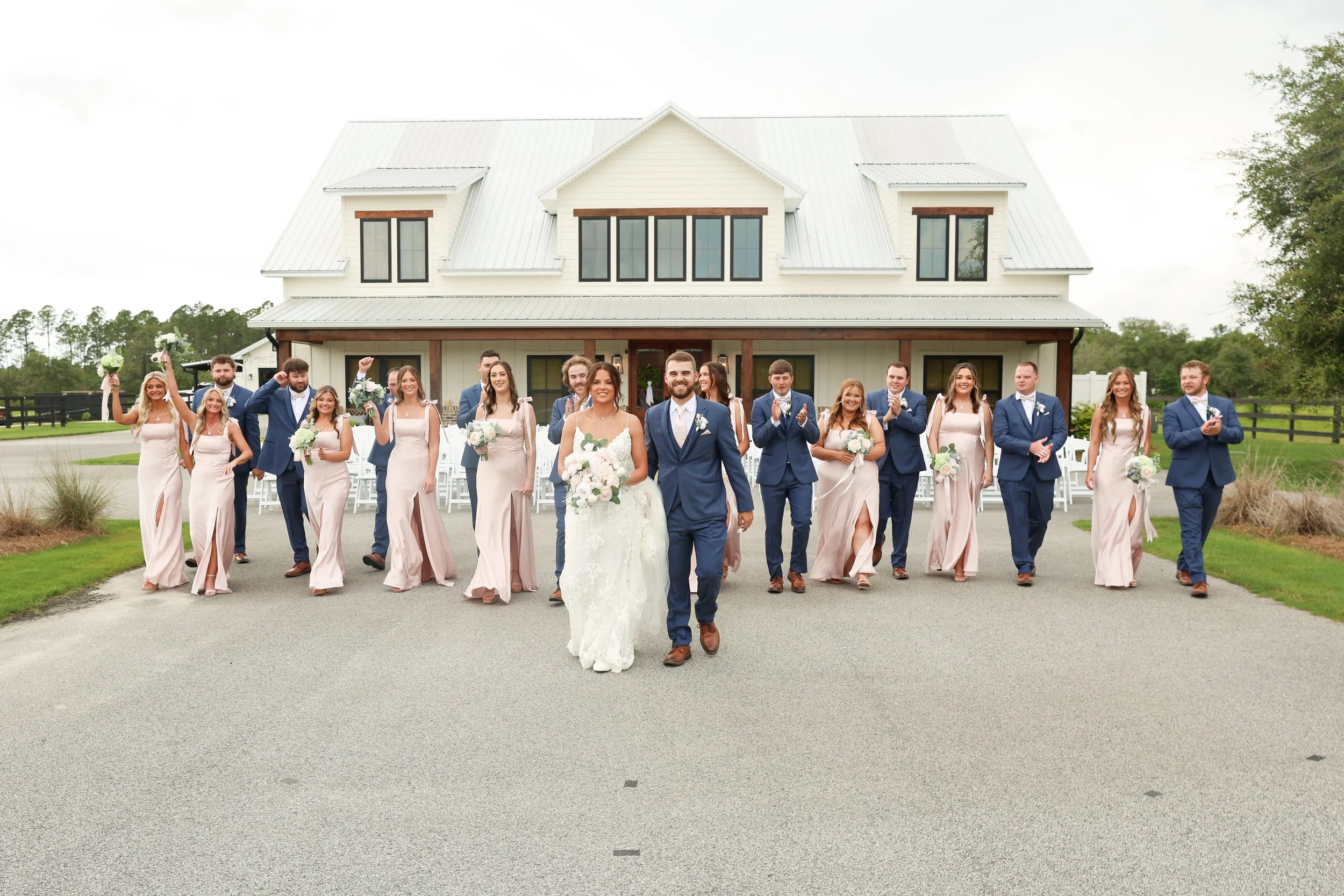 Emma and Dylan lead their wedding party in front of the white barn at Red River Estate in Waynesville, Georgia.