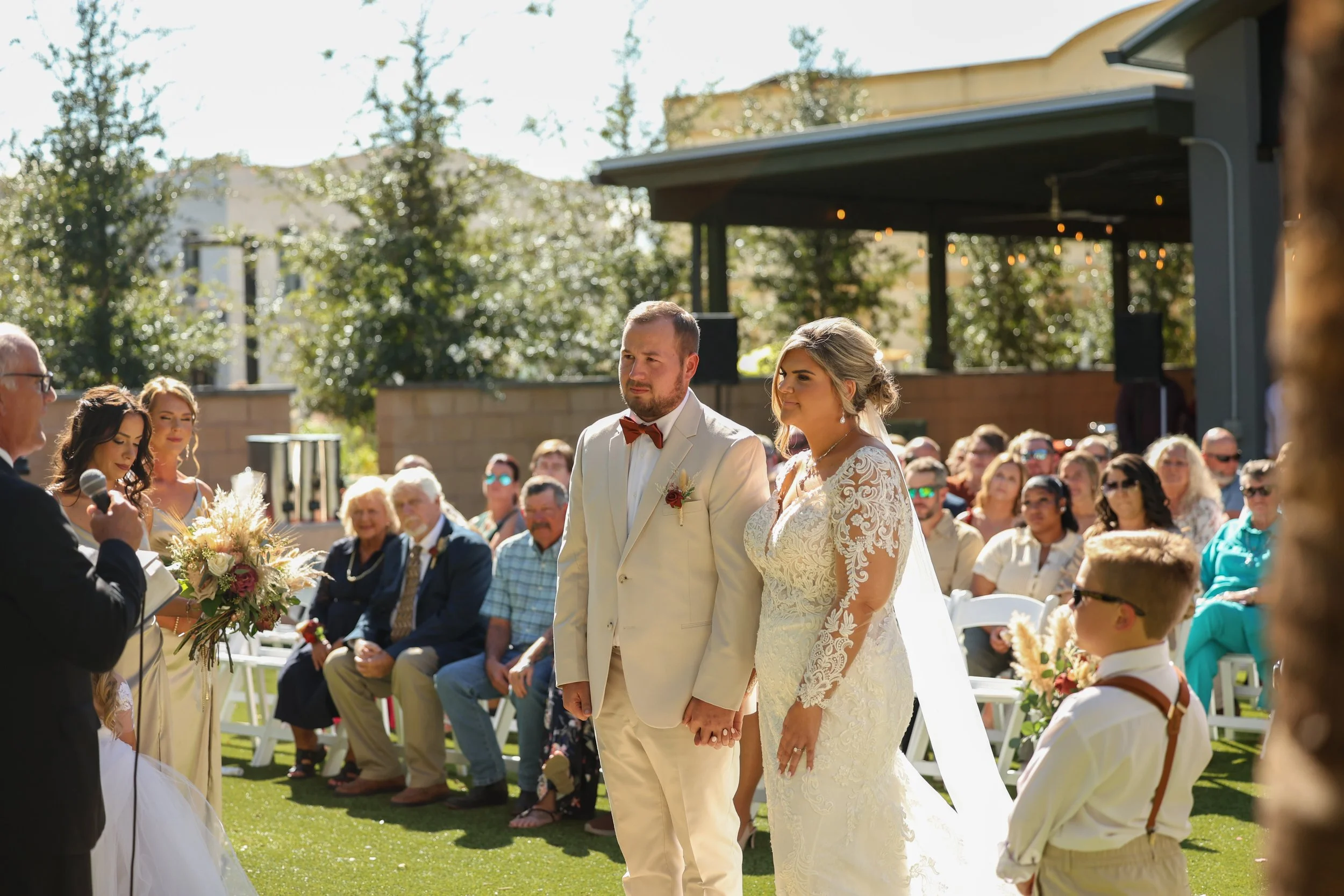 Bride and groom listening during their ceremony while friends and family watch.