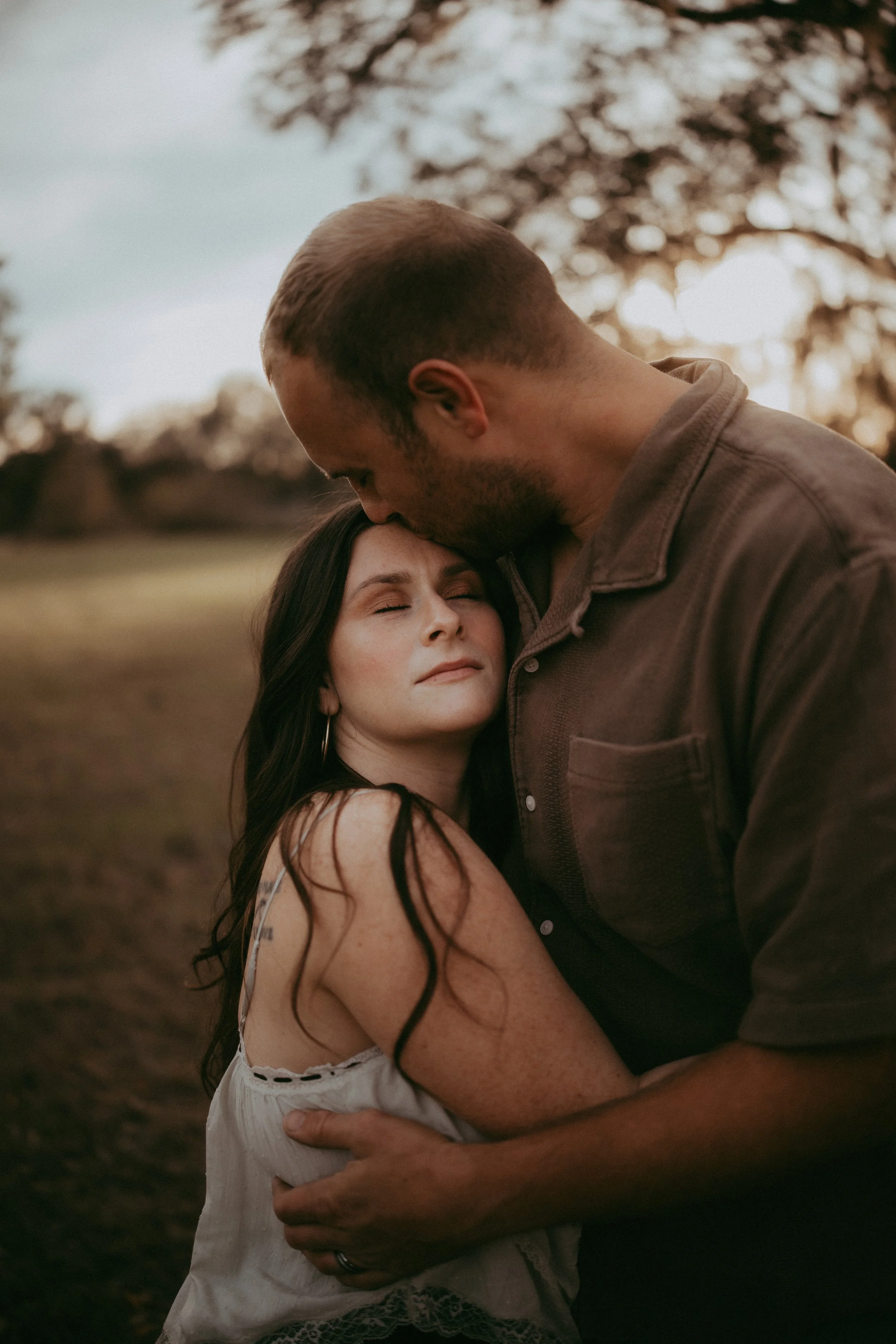 Tender portrait of husband kissing his wife's forehead during a family session, preserving the quiet moments of love that become treasured family memories.