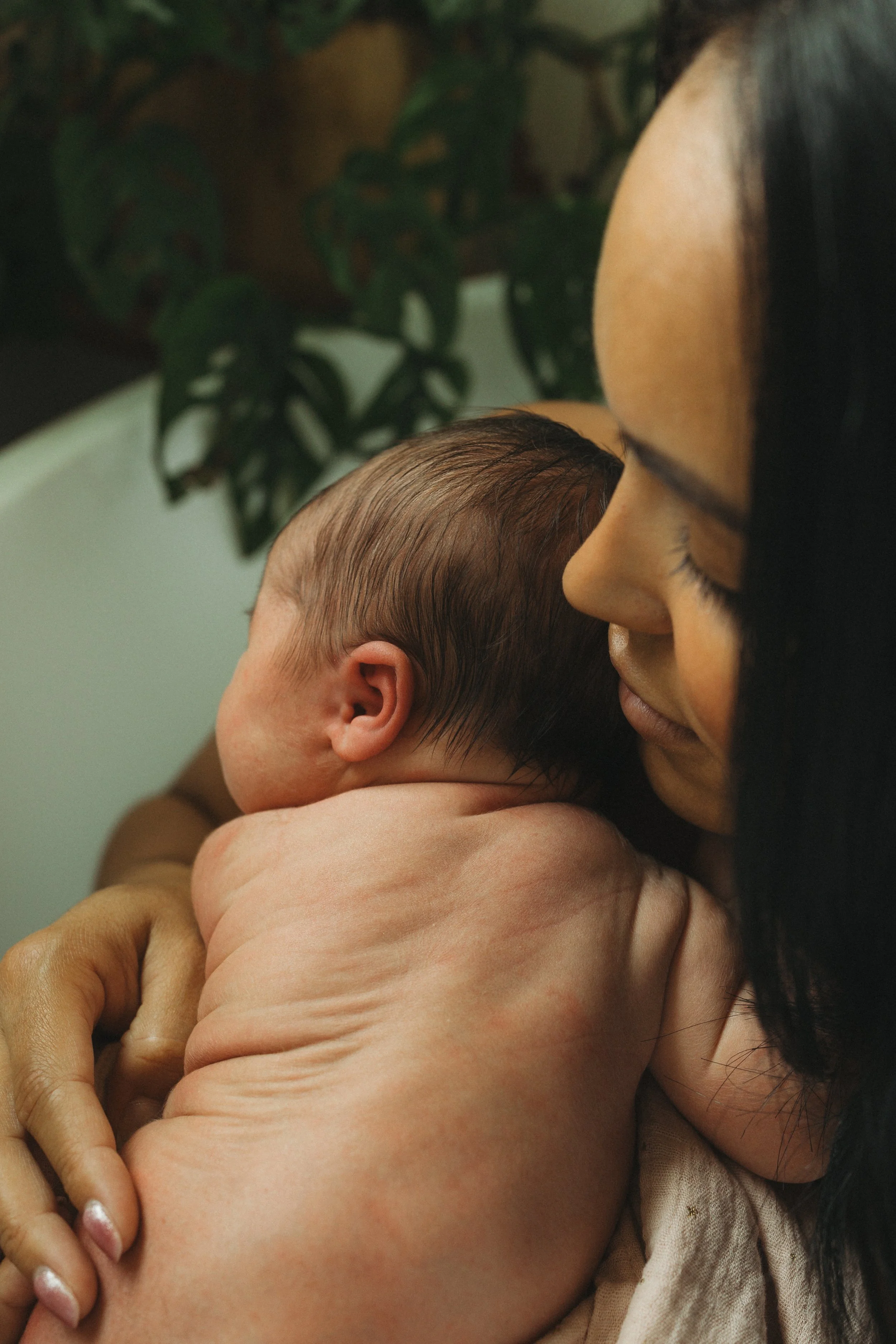 Close-up of a mother holding her newborn against her shoulder, highlighting tiny baby rolls, soft hair, and the comfort of a quiet embrace during an in-home lifestyle newborn photography session.