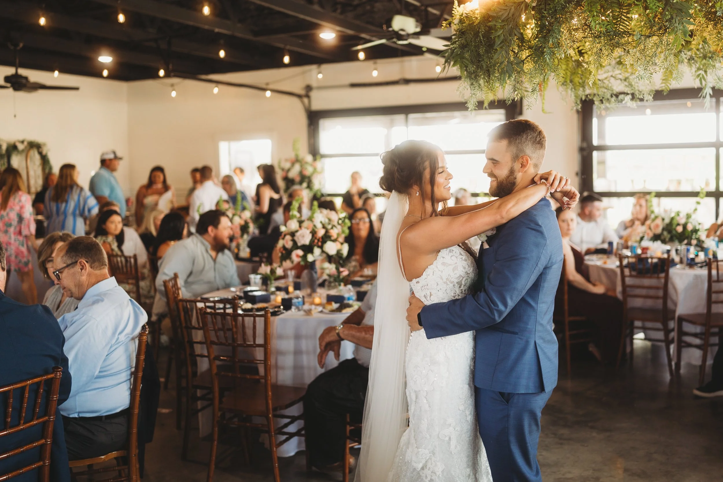 Emmie and Dylan smile at each other during their first dance, surrounded by guests and floral décor at Red River Estate.
