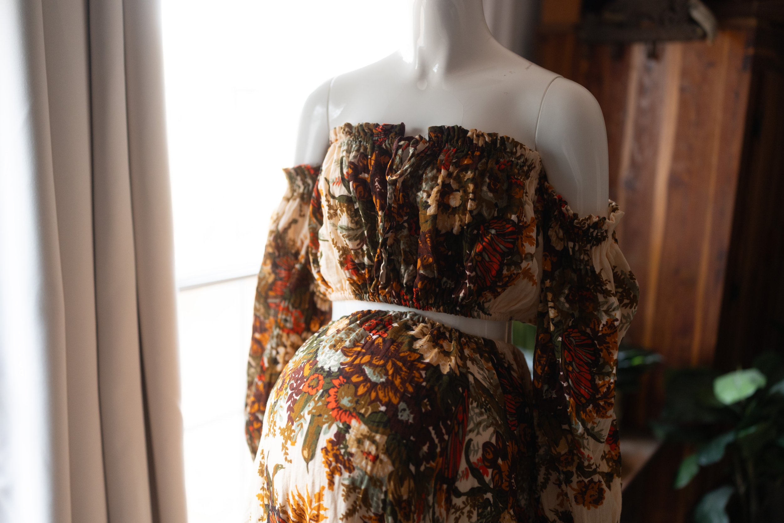 Vintage boho maternity gown in deep rust and olive florals, worn above the belly with dramatic off-shoulder sleeves.