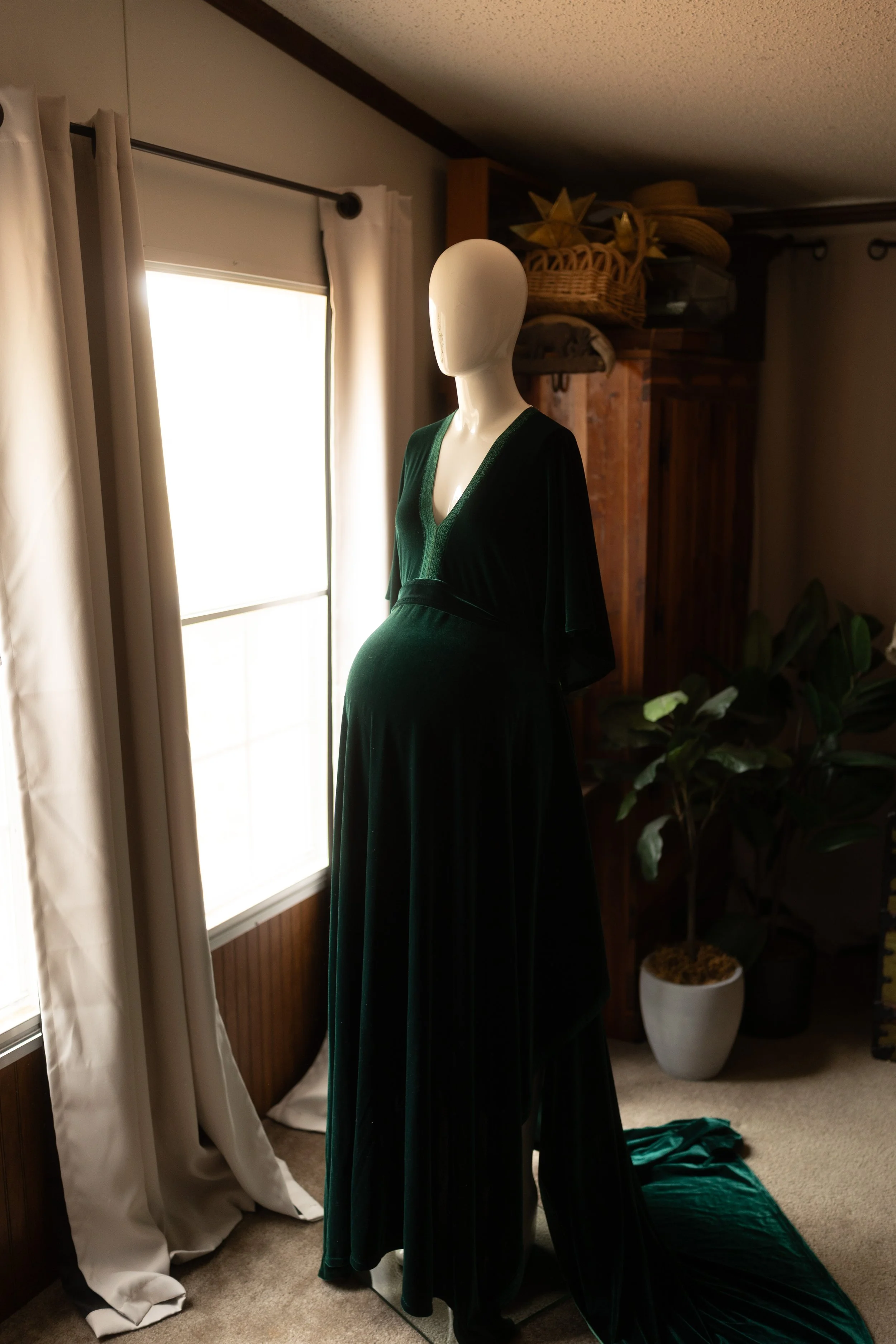 Deep emerald velvet maxi dress with a wrap-style V-neck bodice, long sleeves, and a flowing skirt, styled on a mannequin in soft natural light.
