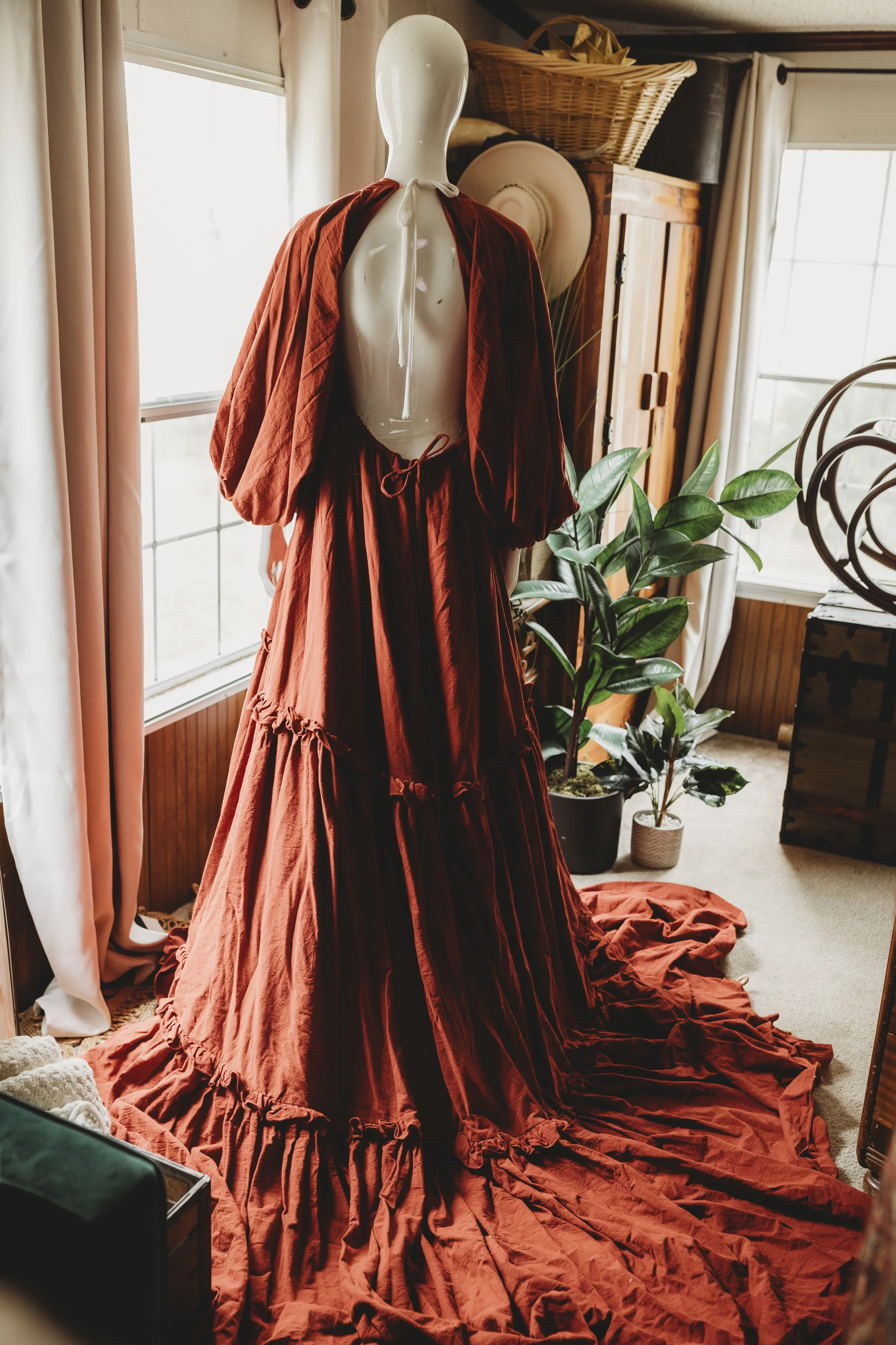 Deep red bohemian maxi dress with an open back, soft tie closure, flowing tiered skirt, and long sleeves, displayed on a mannequin in natural window light.