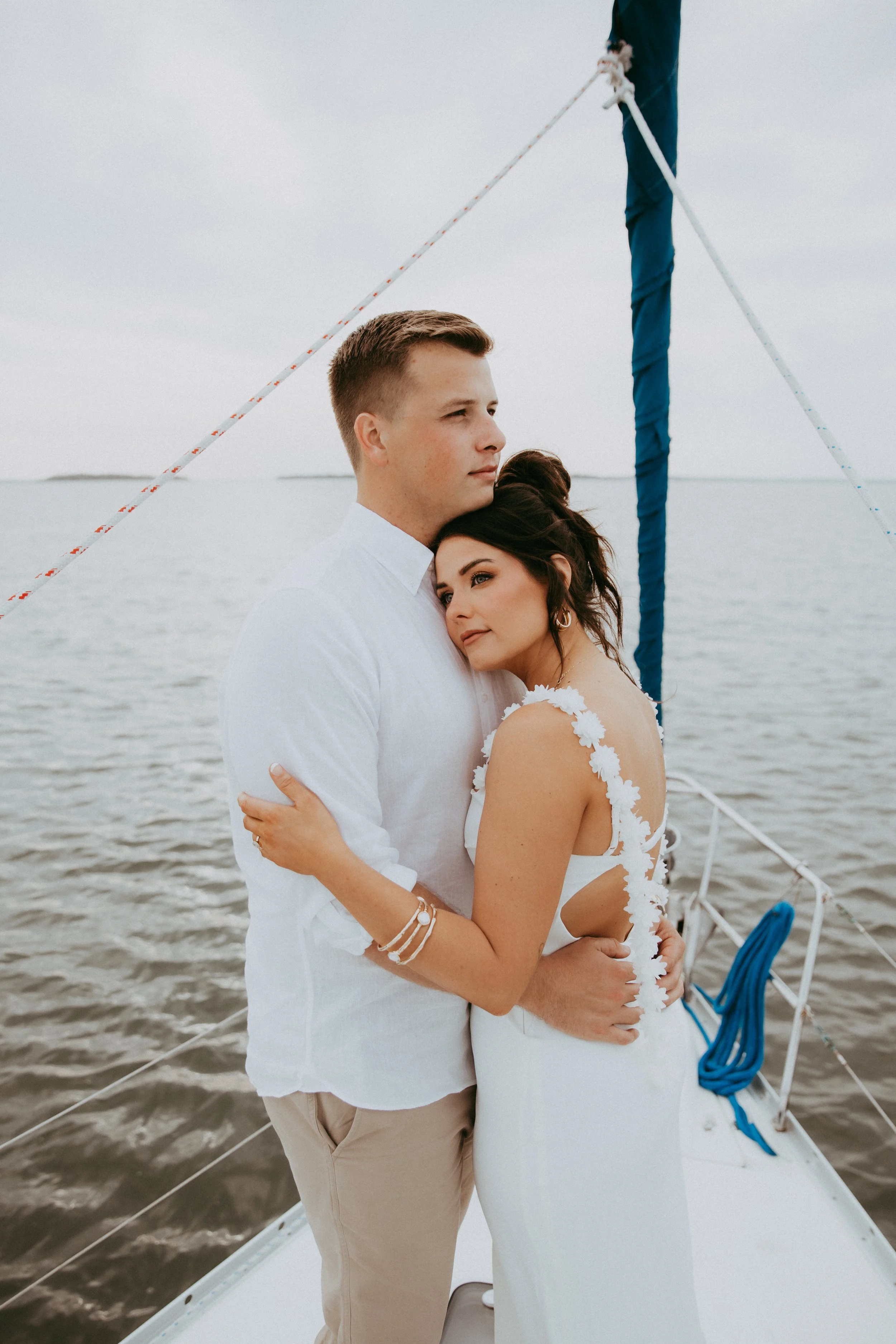 Lyndsey and Adam stand close together against an overcast sky and open water