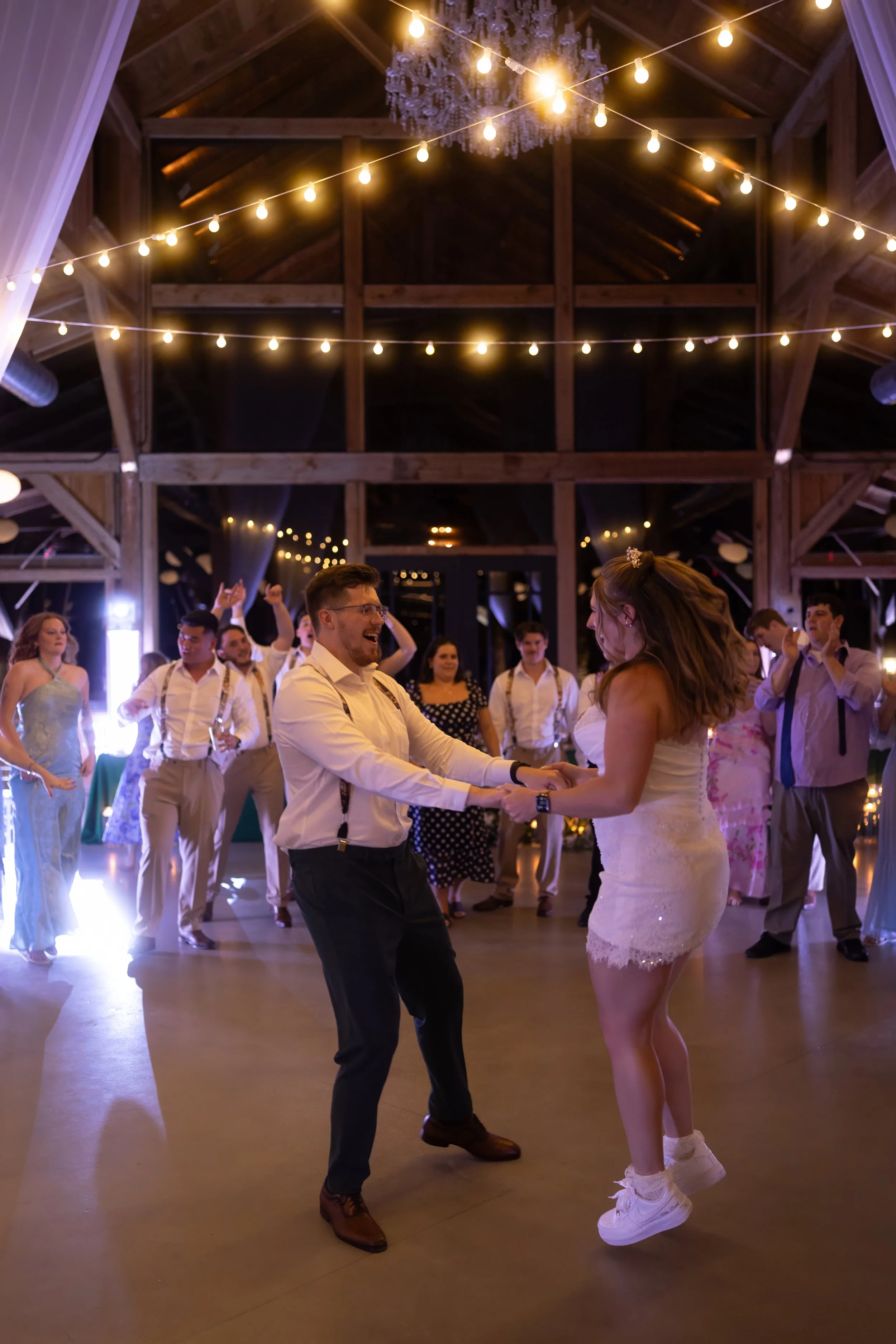 Bride and groom laugh and sing together while dancing with guests during their lively wedding reception.