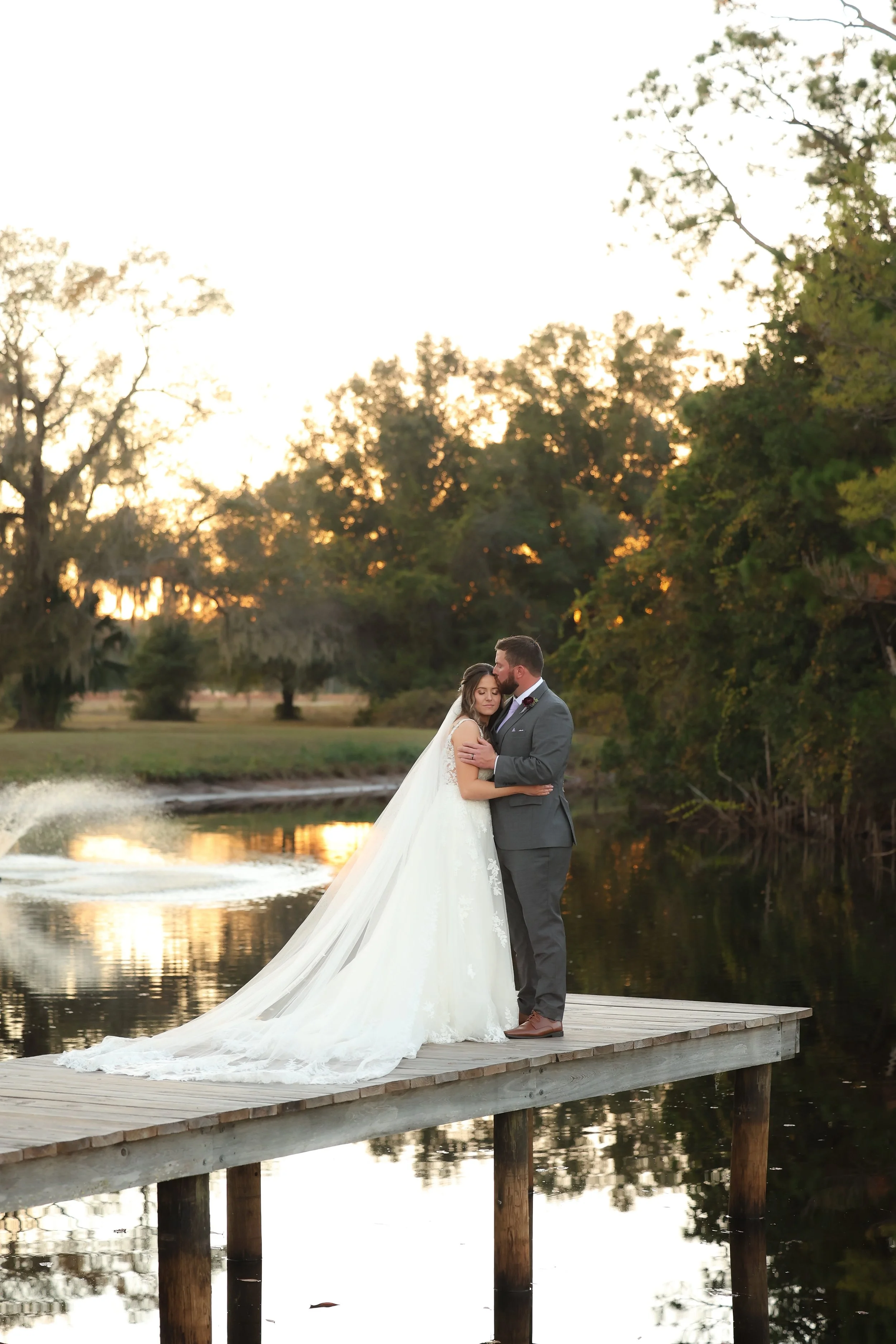 Bride and groom embracing on a wooden dock beside a pond at sunset during their Northeast Florida wedding.