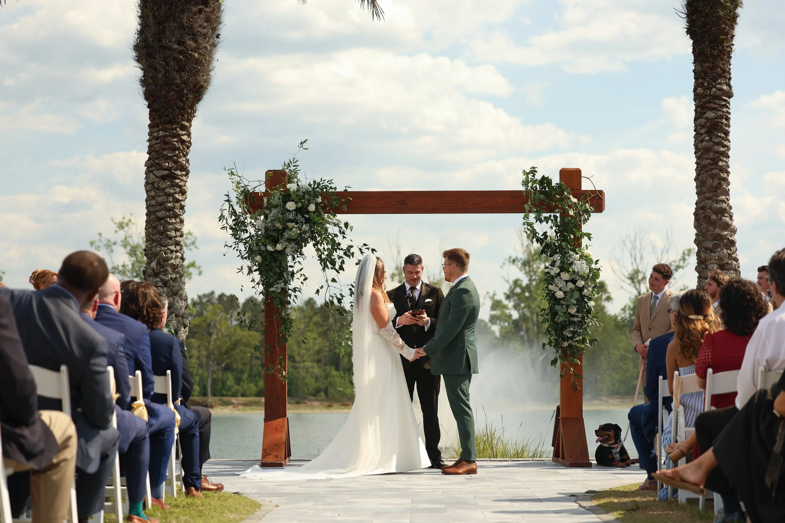 Bride and groom exchange vows beneath a floral arbor overlooking the lake during their outdoor Cottonwood Ranch wedding ceremony.