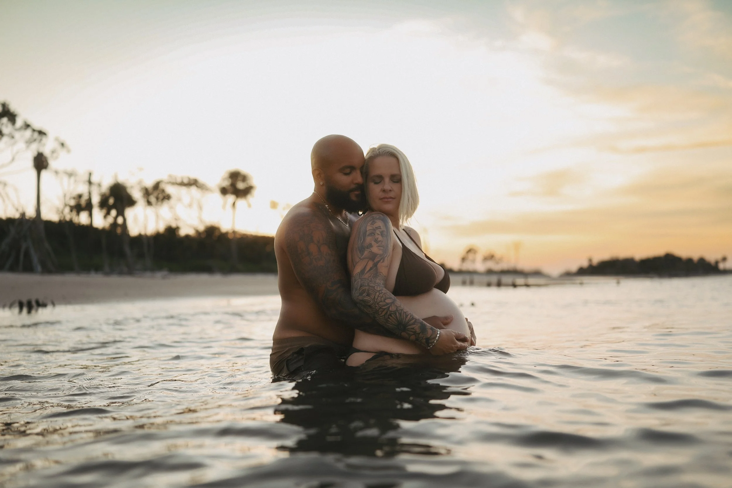 Sunset maternity photo of an expectant couple sharing a peaceful embrace in the water as they await their baby.