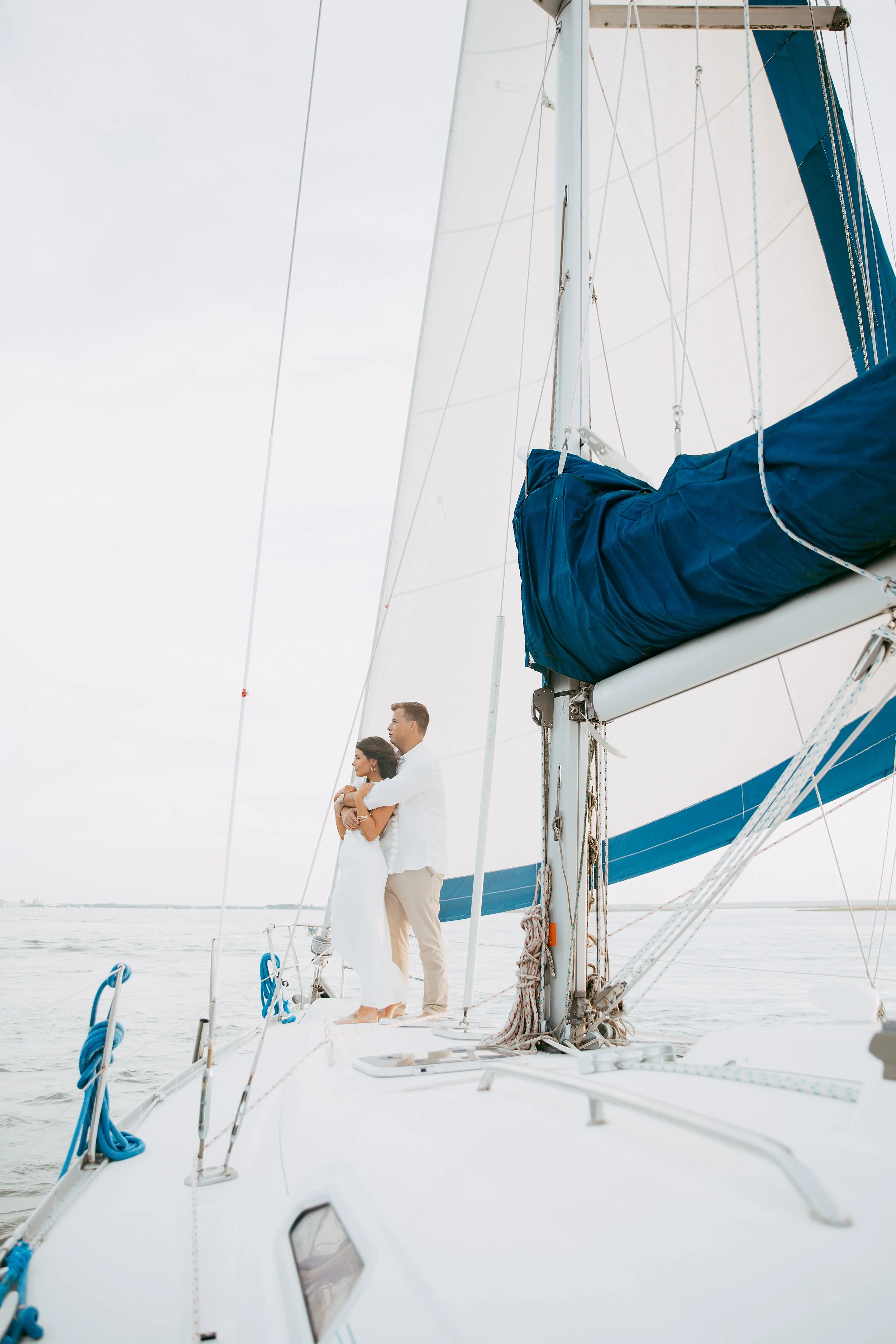 Wide portrait of Lyndsey and Adam embracing beneath the tall blue-and-white sails