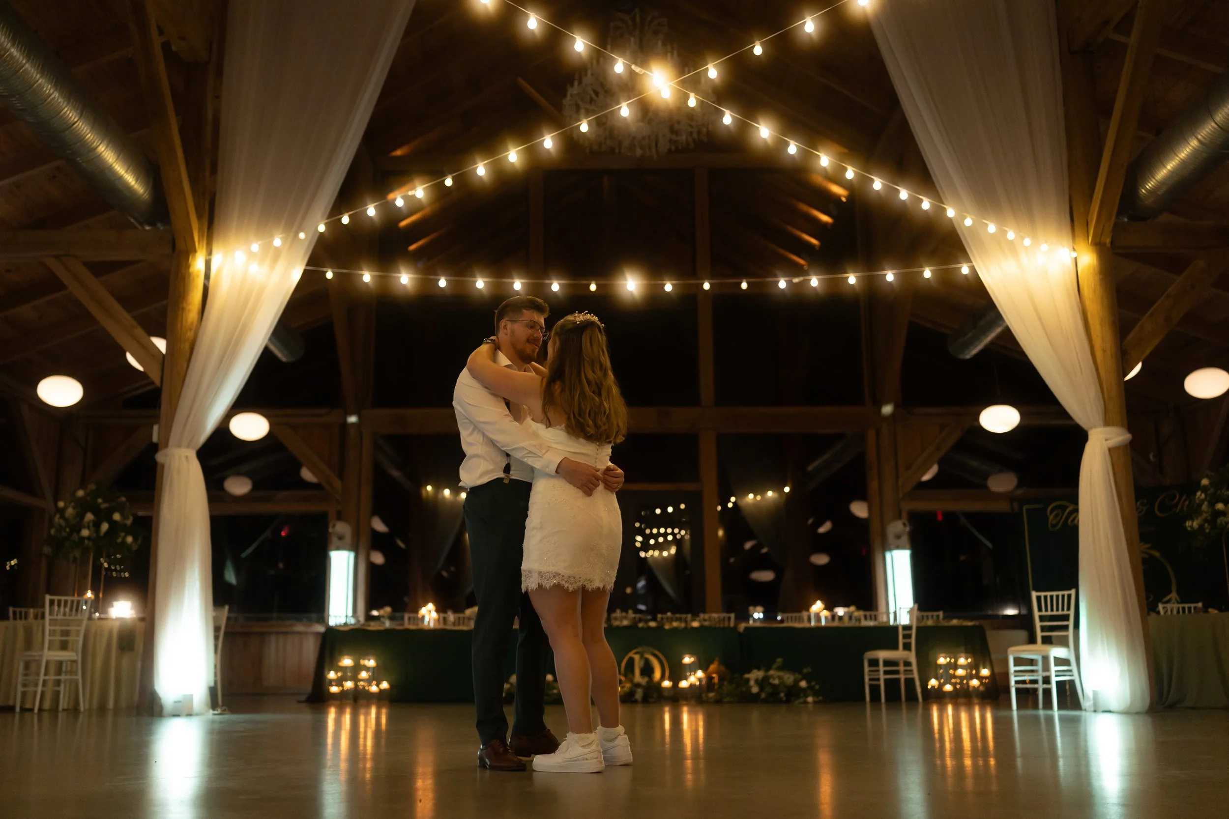 The bride and groom share a quiet dance beneath twinkling lights at the end of their wedding day.
