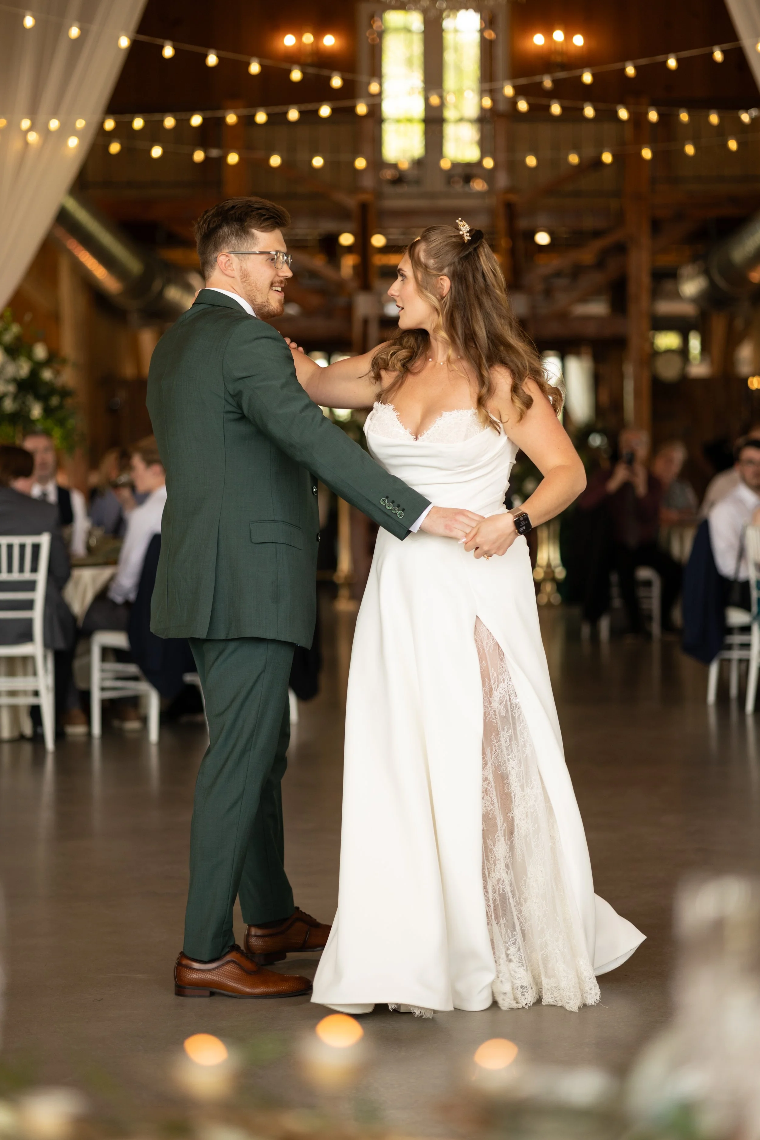 The newlyweds share their first dance beneath glowing string lights inside Cottonwood Ranch.