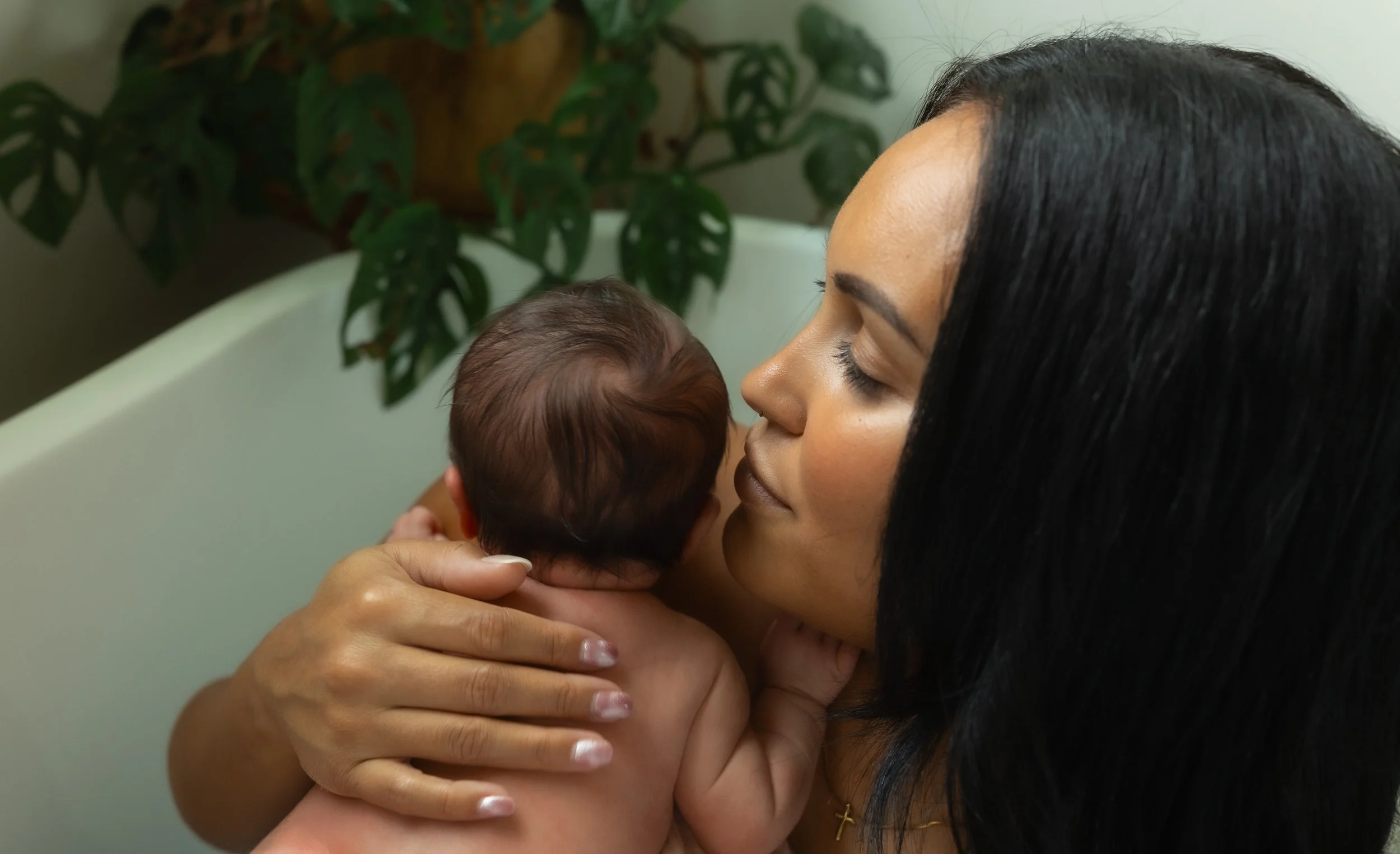 Mother gently holds her newborn against her shoulder and nuzzles close, capturing a tender skin-to-skin inspired moment filled with warmth, comfort, and connection during an in-home lifestyle newborn photography session.