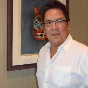 A man wearing glasses and a white shirt, standing in front of a framed painting.