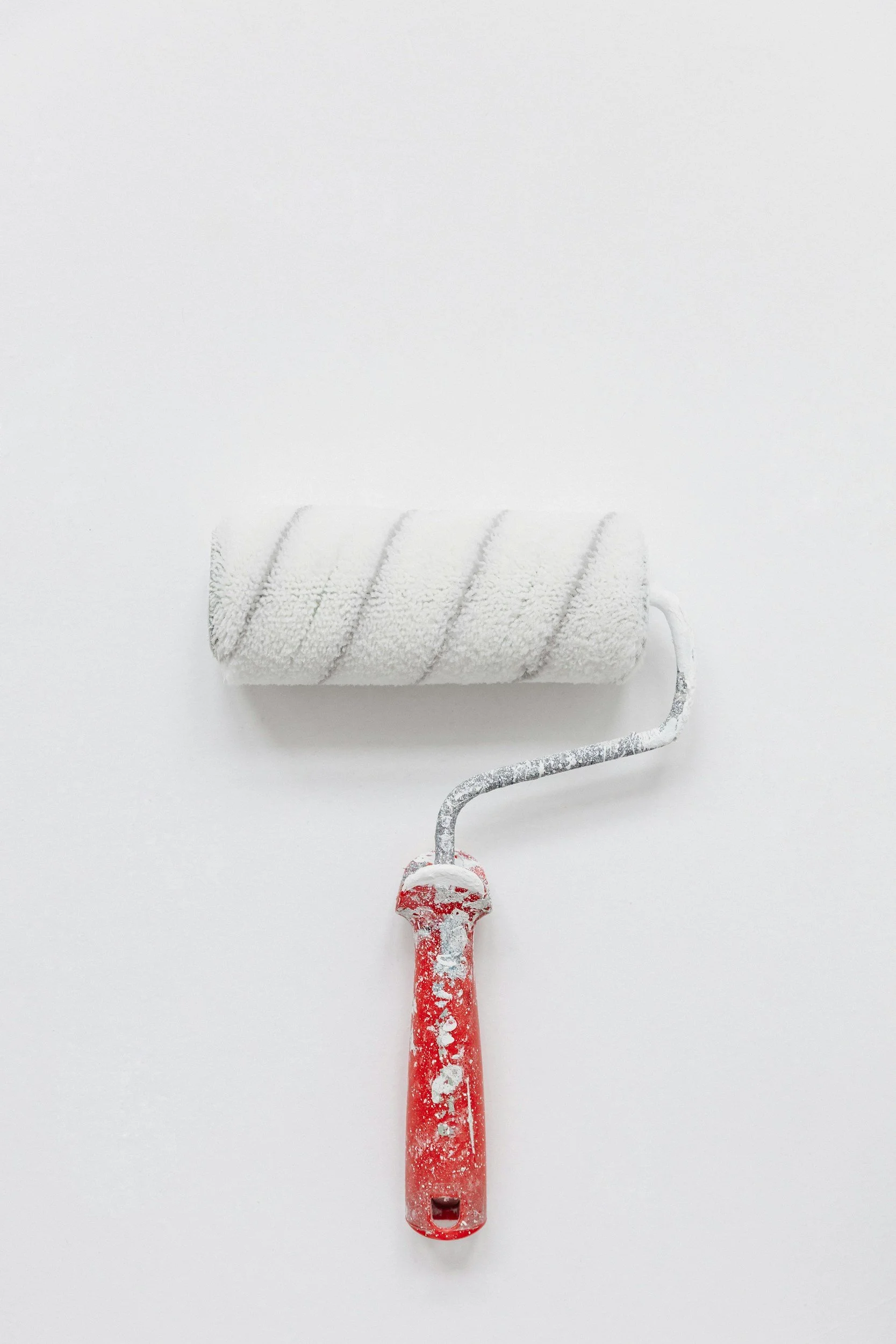 A paint roller covered in white paint with a red handle, resting on a white surface.