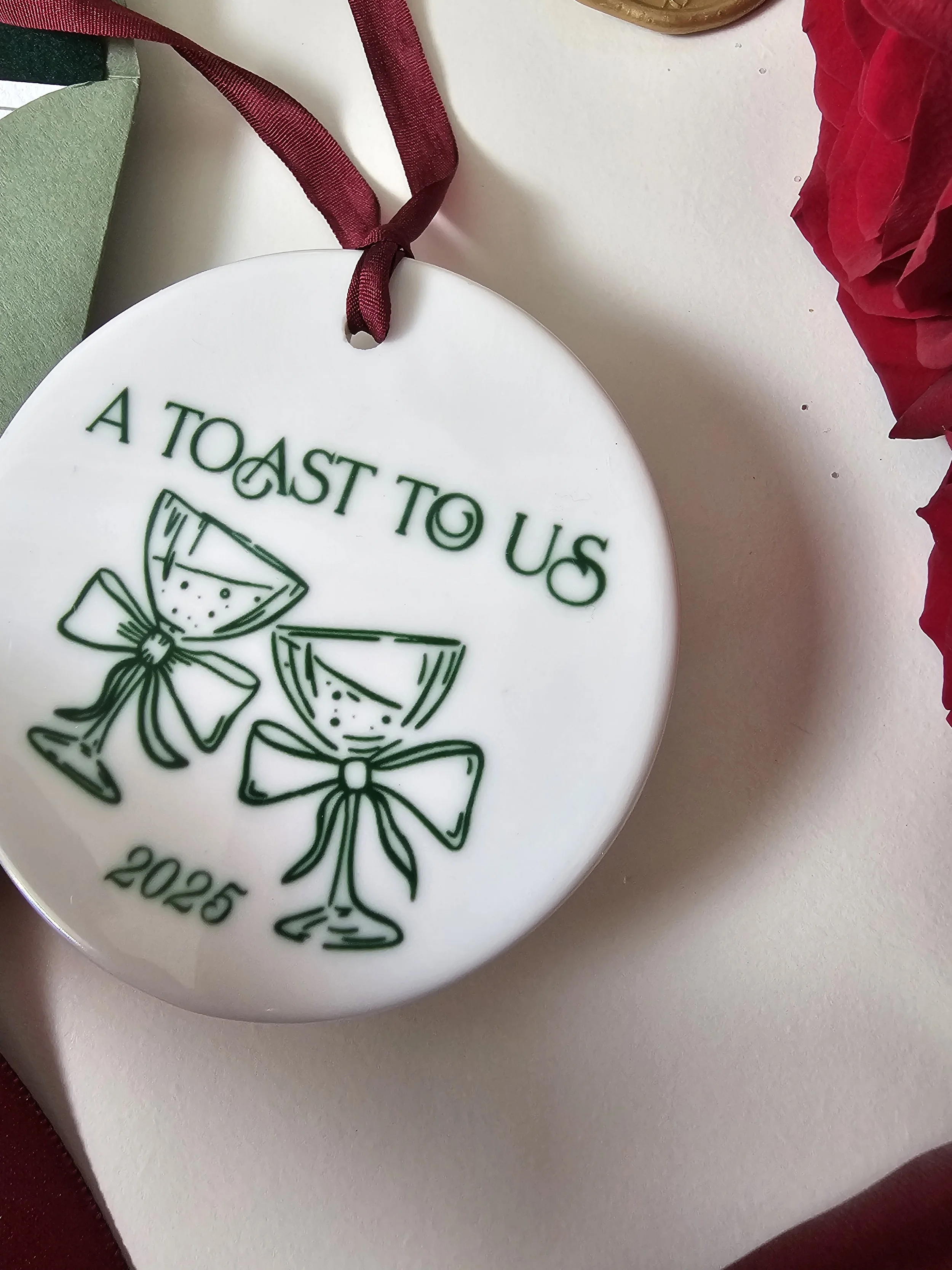 Close-up of 2025 Toast to Us ceramic holiday ornament with coupe glasses illustration