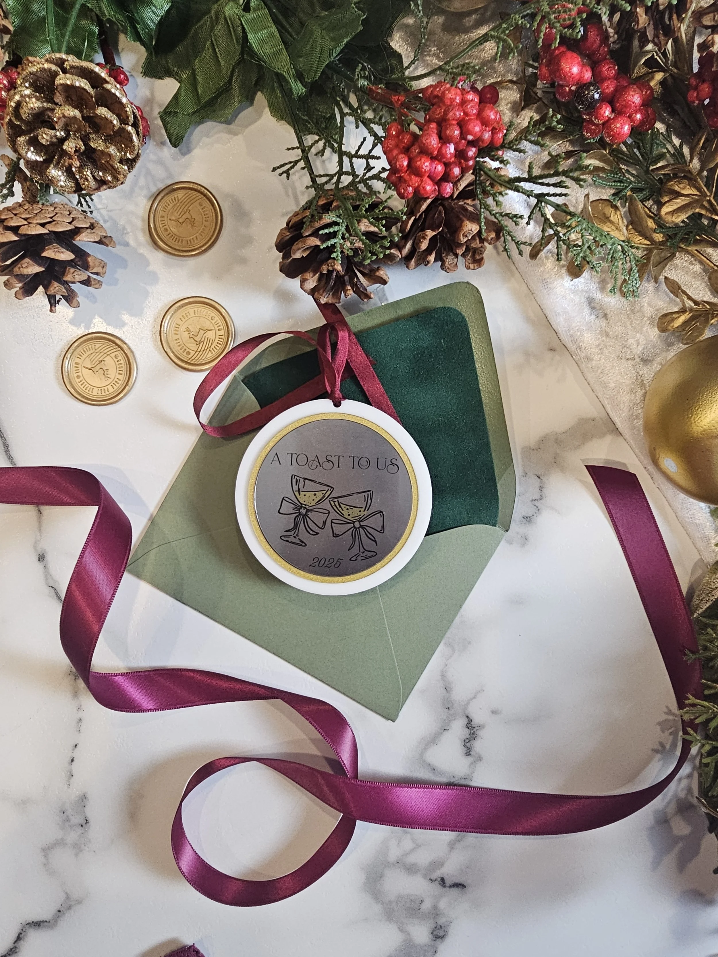 “A Toast to Us” couples ornament with champagne glasses, burgundy ribbon, and green envelope styling