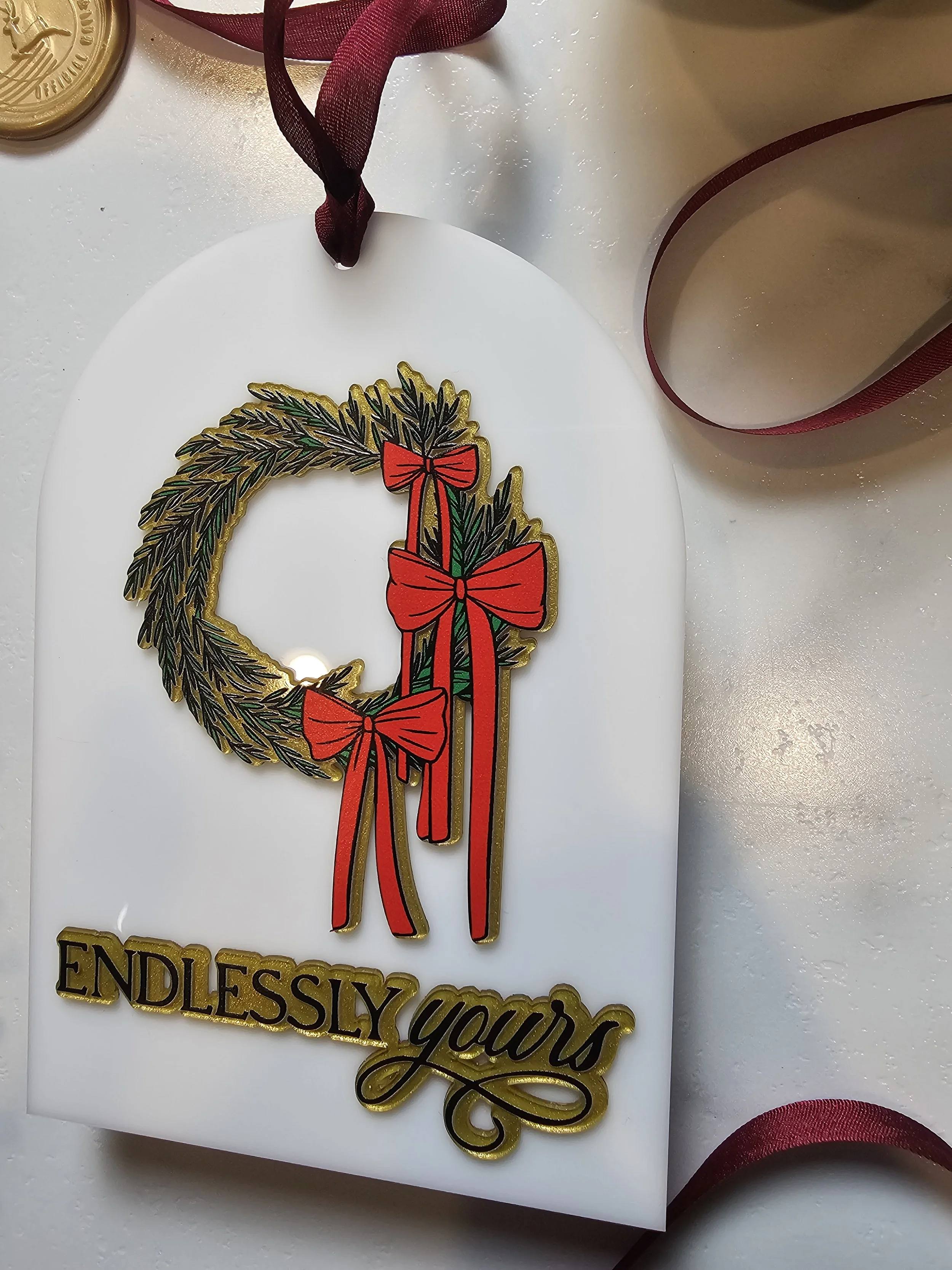 Close-up of Wreath Heirloom Ornament with red bows and gold embossed “Endlessly Yours” lettering