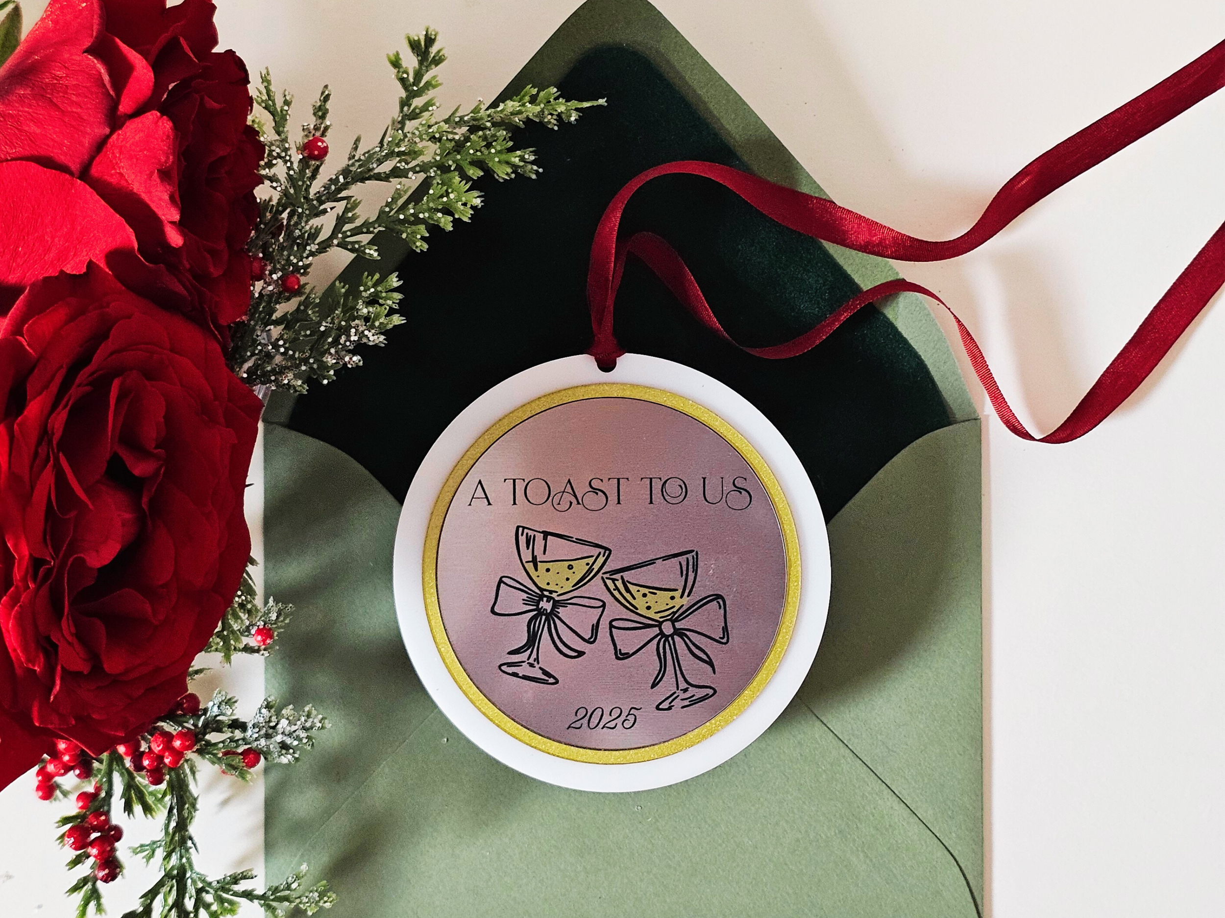 White acrylic 2025 champagne toast ornament displayed with roses and winter greenery