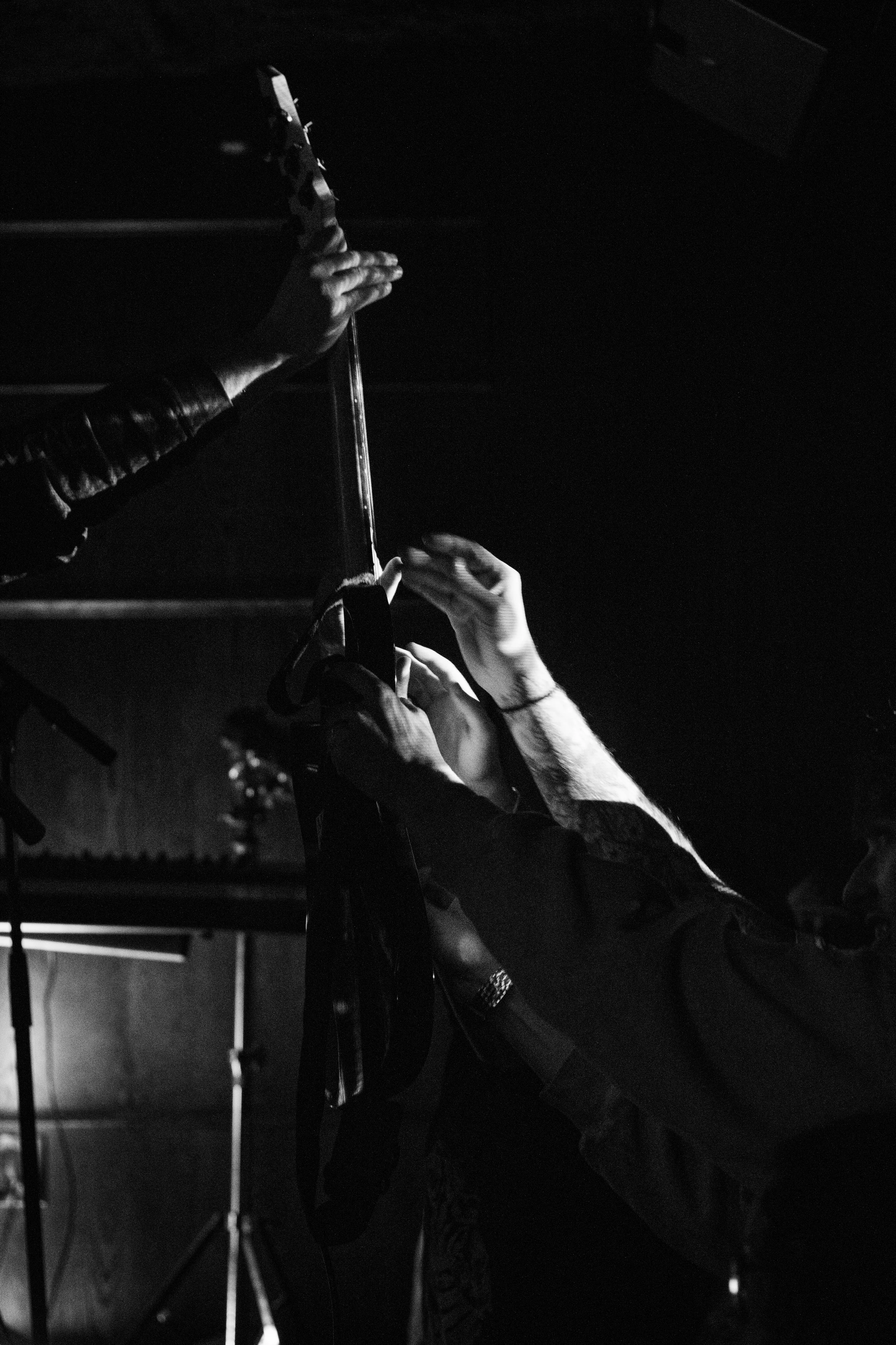 Black and white photo of a person holding their guitar out to a crowd in a dark room.