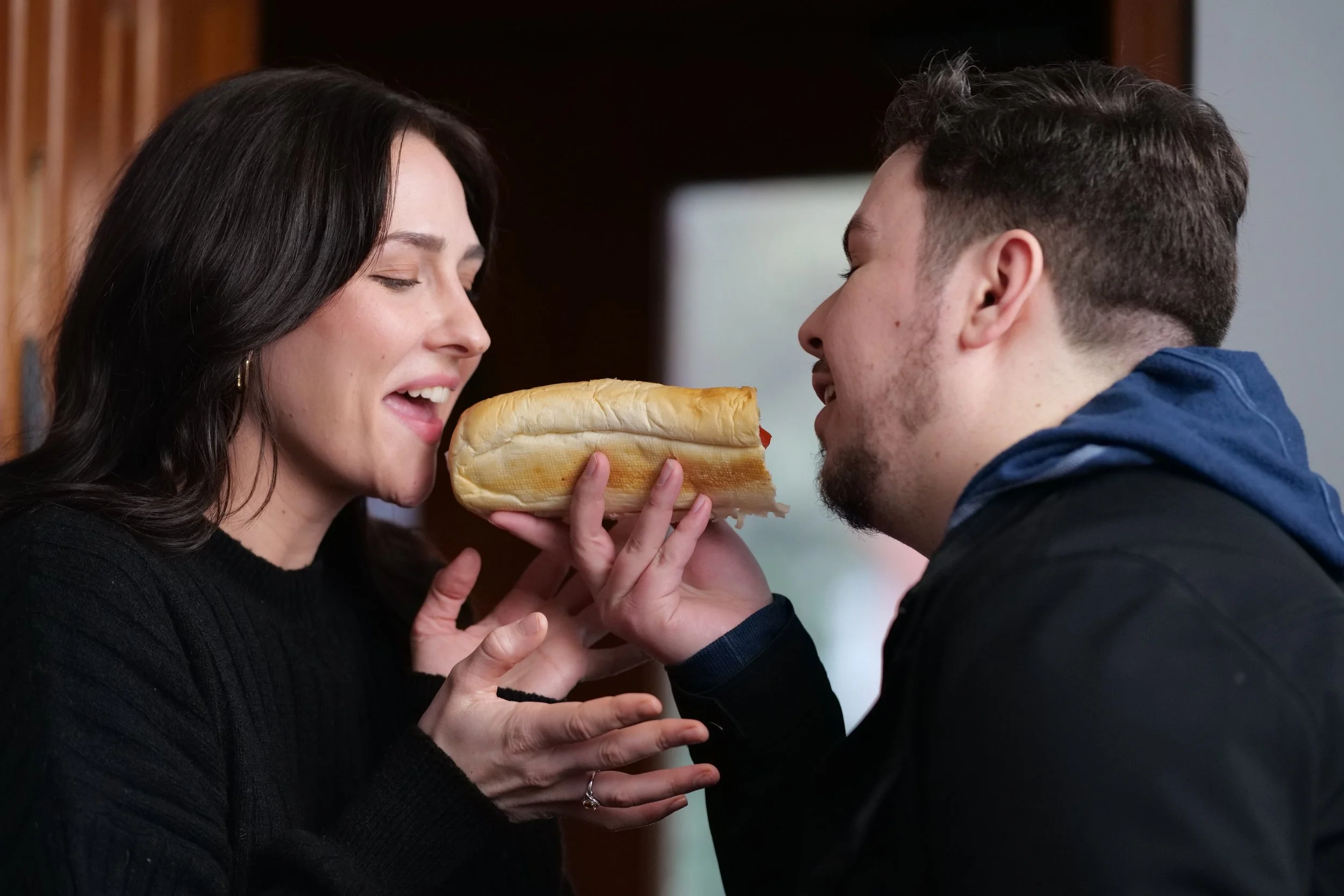 A woman and a man are holding a sub sandwich together, both about to take a bite "Lady and the Tramp" style. Jordan Black & Stephanie Robertson