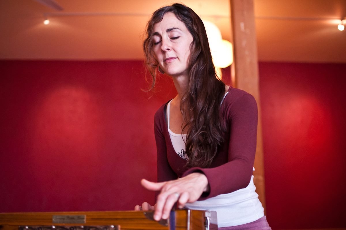 A yoga teacher with a peaceful look on her face plays a harmonium instrument in a yoga studio