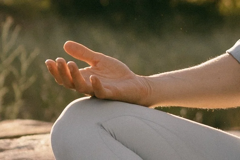 Close-up of a person's hand in a meditative mudra gesture, resting on their knee during sunrise or sunset outdoors.