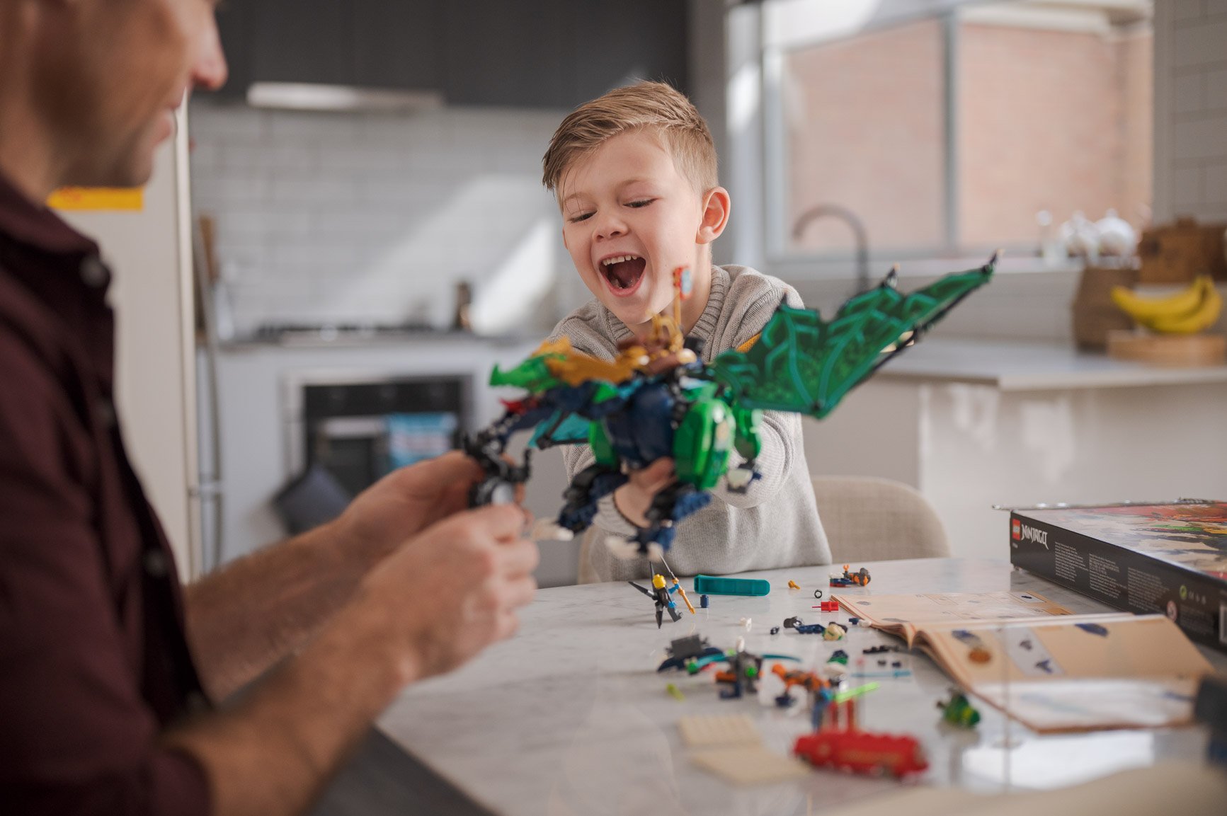 Father and son playing with a LEGO dragon set at the kitchen table.