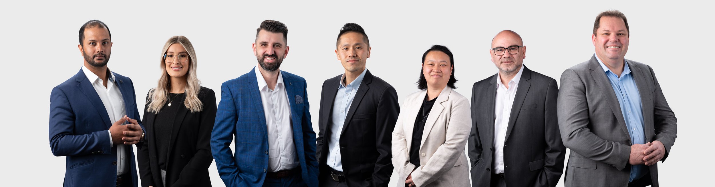 Group of seven professionally dressed individuals standing against a plain background.