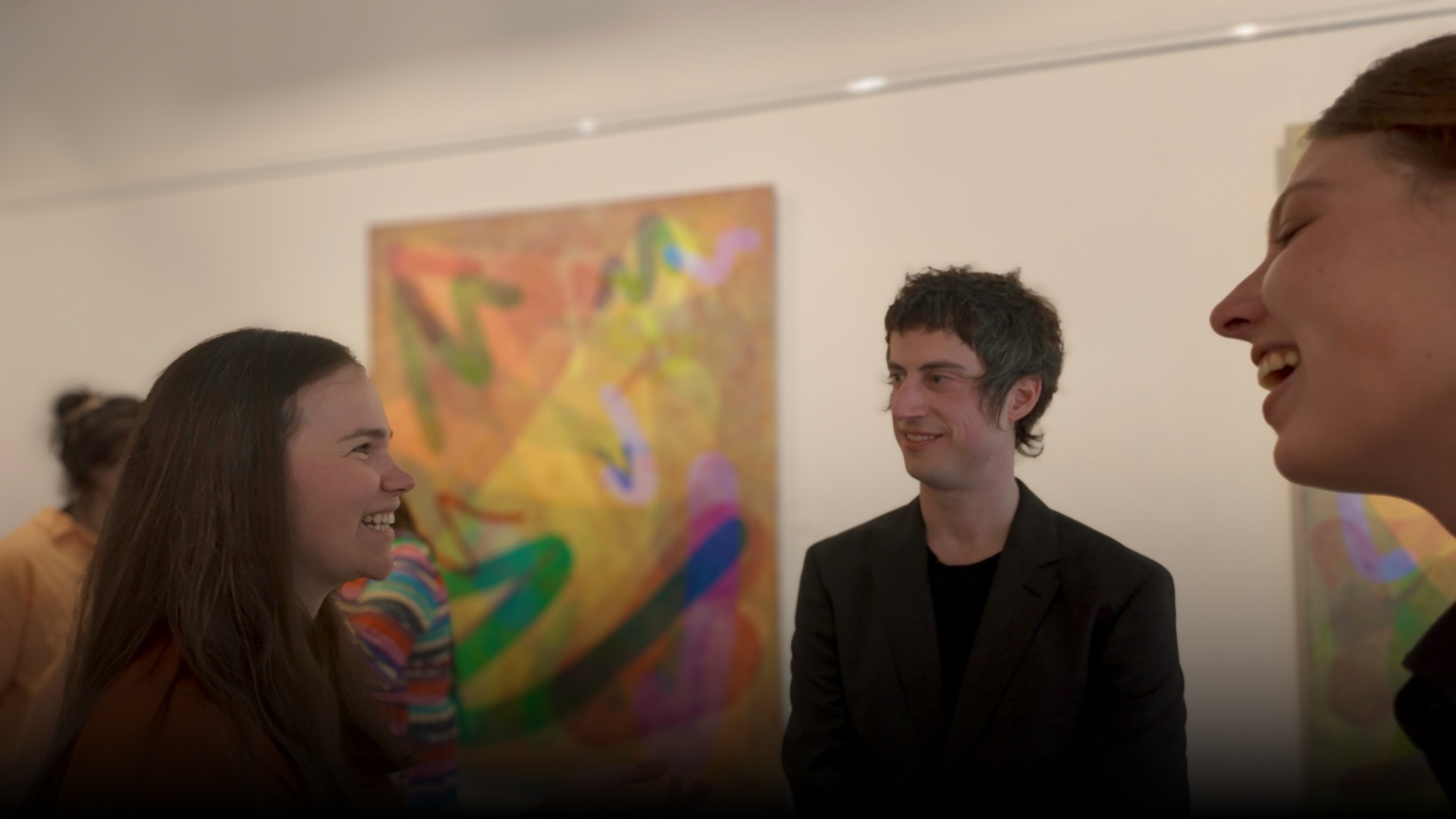 Group of four people smiling and talking at an art gallery with colorful abstract paintings in the background.