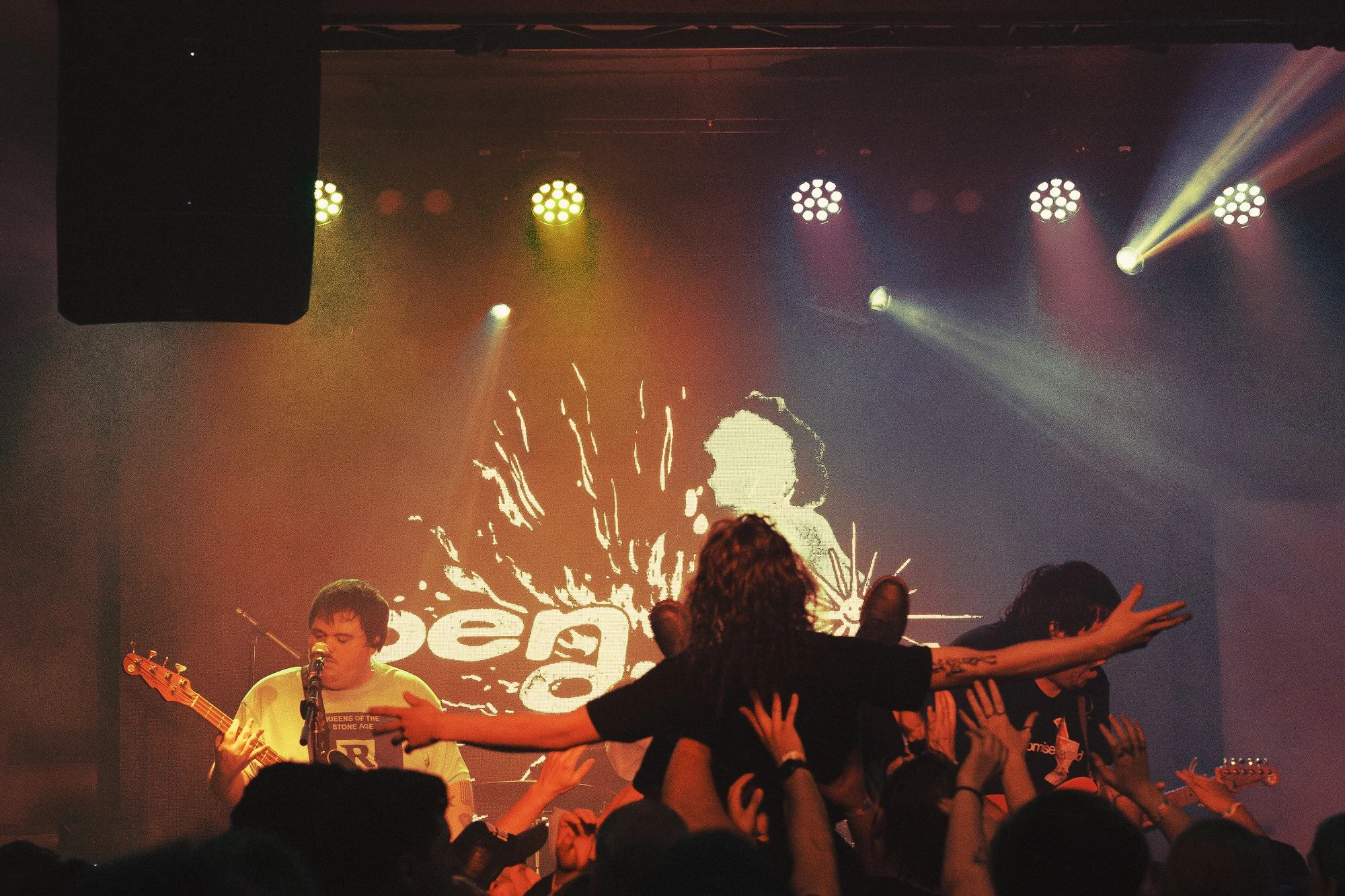 Band performing on stage in a concert with colorful lighting. Crowded audience reaching out to the performers.