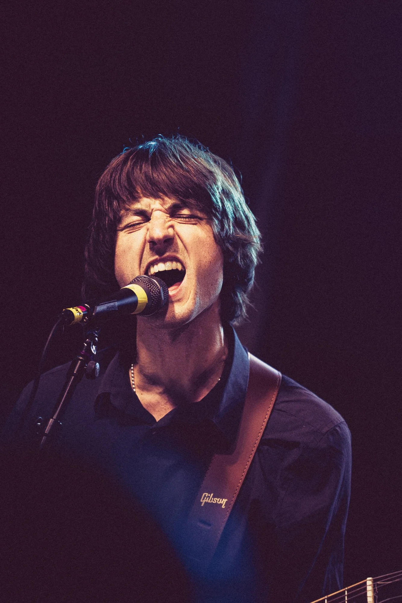 A man singing passionately into a microphone while playing a Gibson guitar on stage.