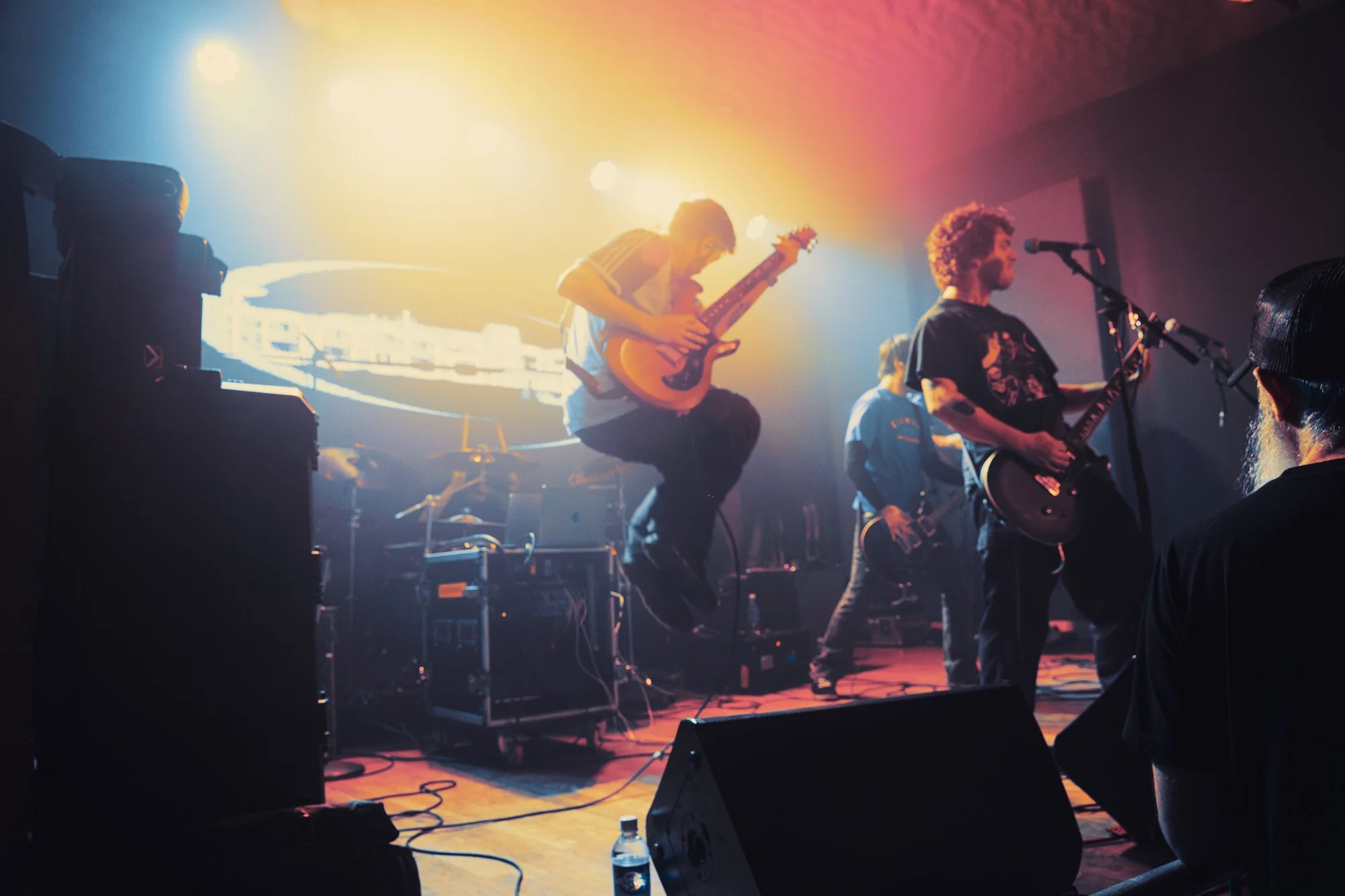 Musicians performing on stage with colorful lighting and stage equipment, including guitars and amplifiers.