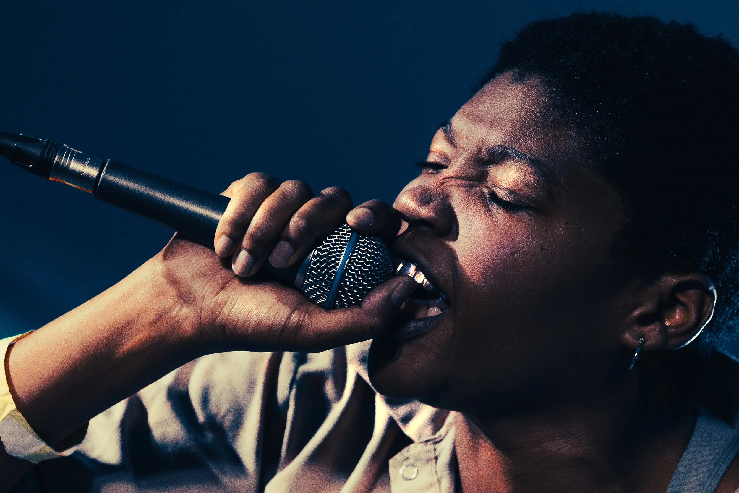 Close-up of a woman singing passionately into a microphone with her eyes closed.