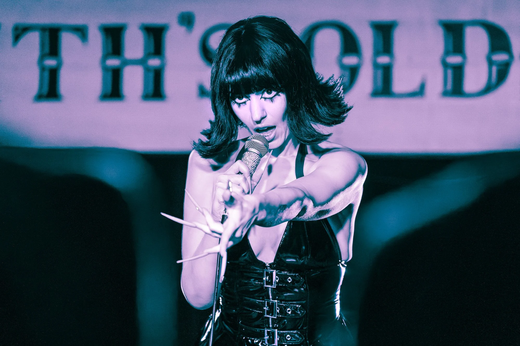 A woman with black hair and bangs singing into a microphone on stage with a blurry background.
