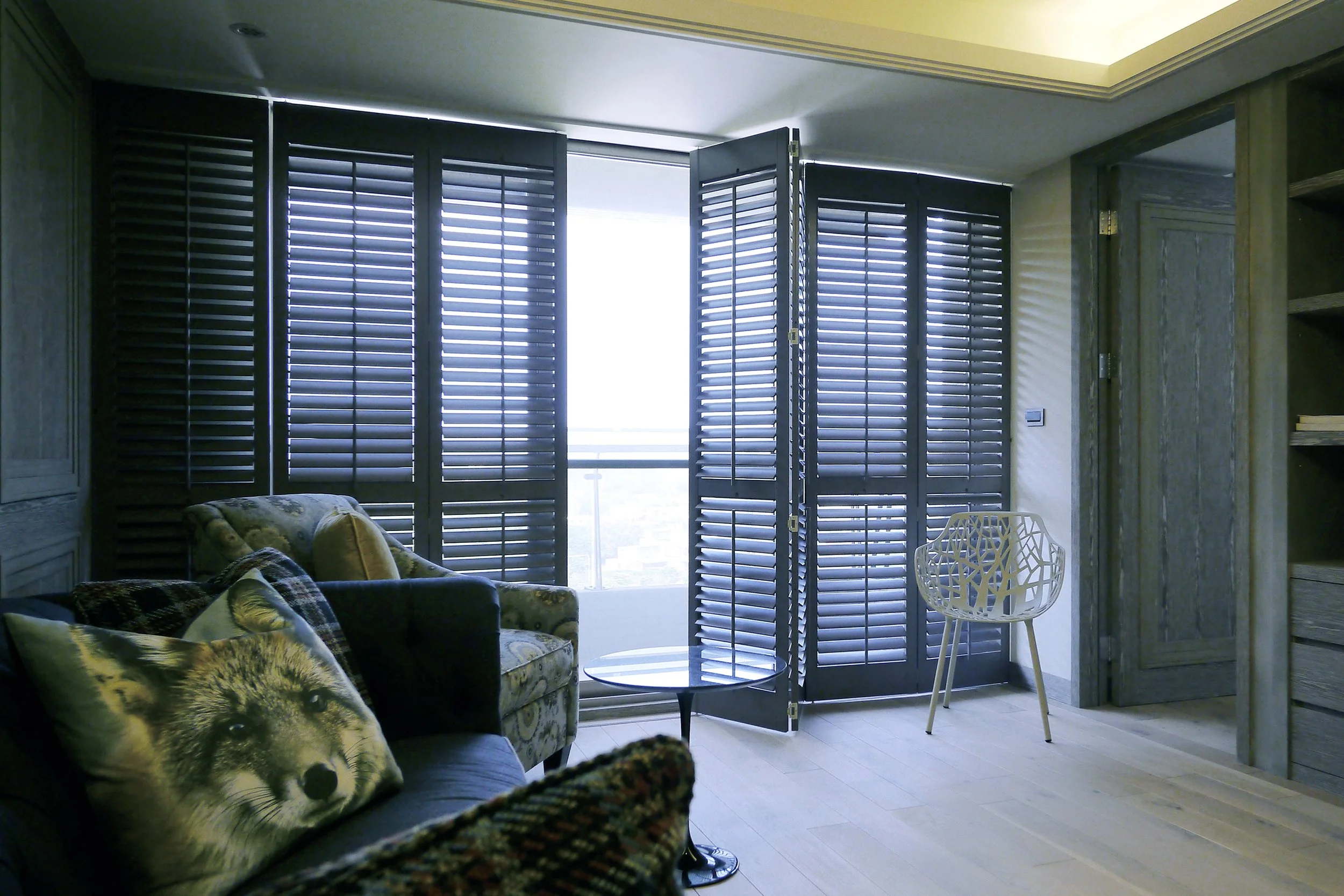 Custom dark plantation shutters covering large living room windows with adjustable louvers and folding panels.