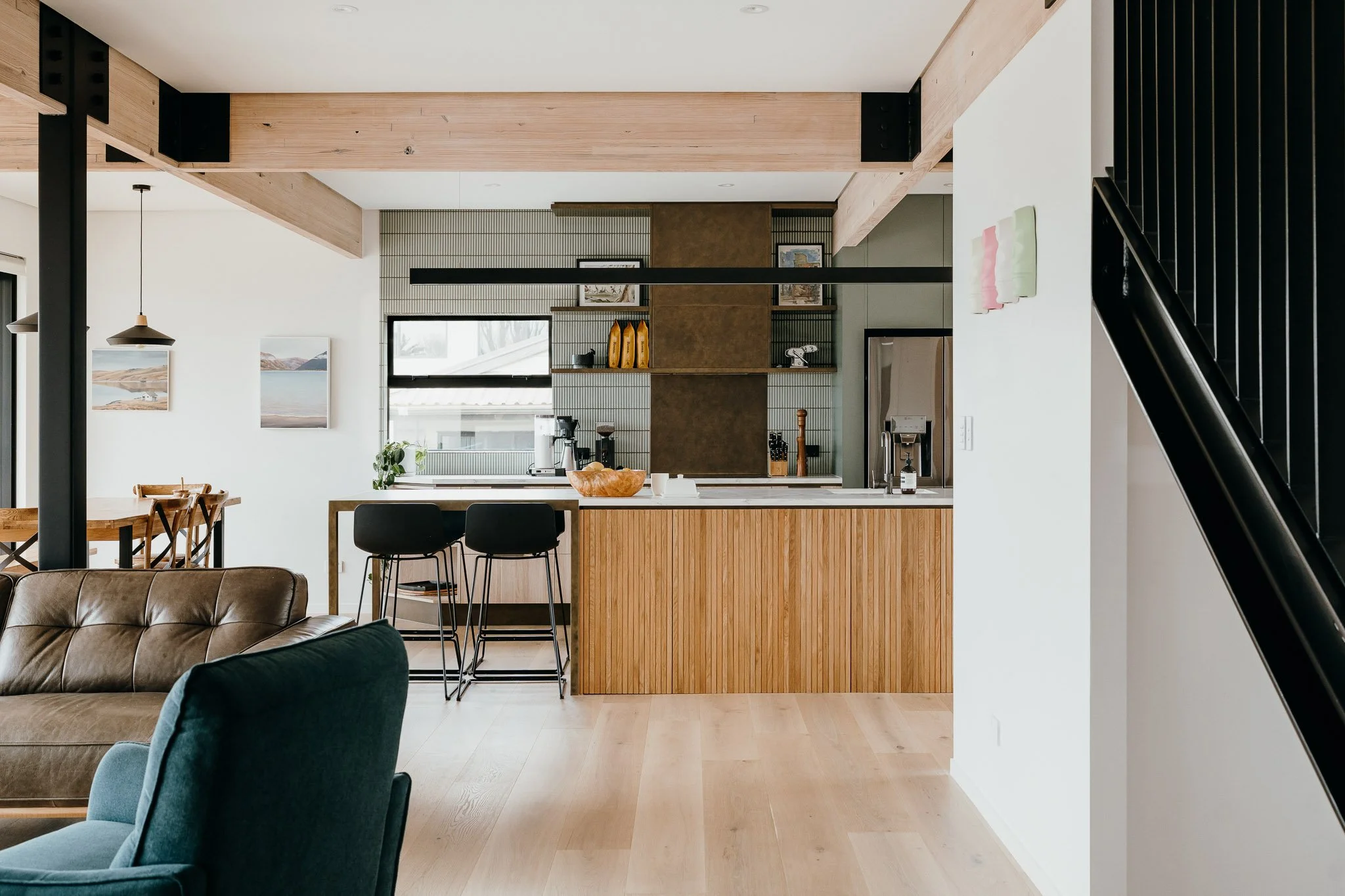 Modern kitchen and living area with wooden accents, a bar with stools, brown and blue seating, open shelves, and a dining table with chairs.