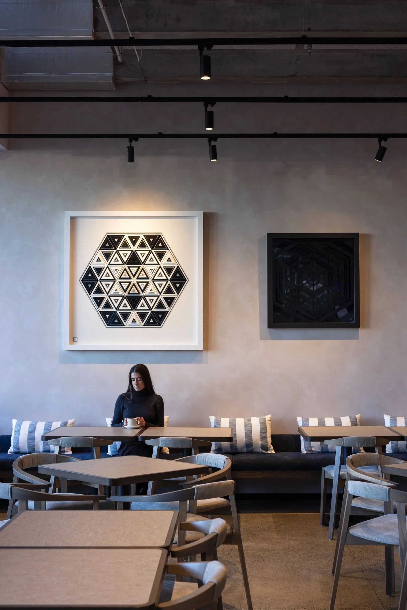 A woman sitting at a table in a modern, minimalistic cafe with geometric art on the wall