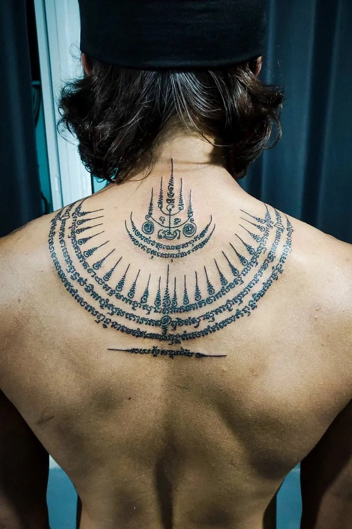 A man wearing a hat with a bambo sak yant on his upper back