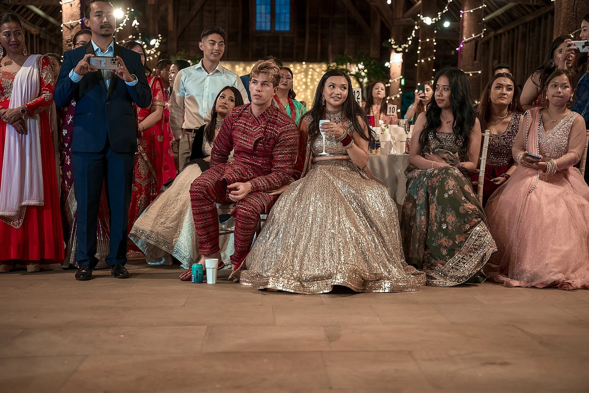 People dressed in traditional Indian attire at a celebration or wedding event inside a decorated venue with string lights and tables.