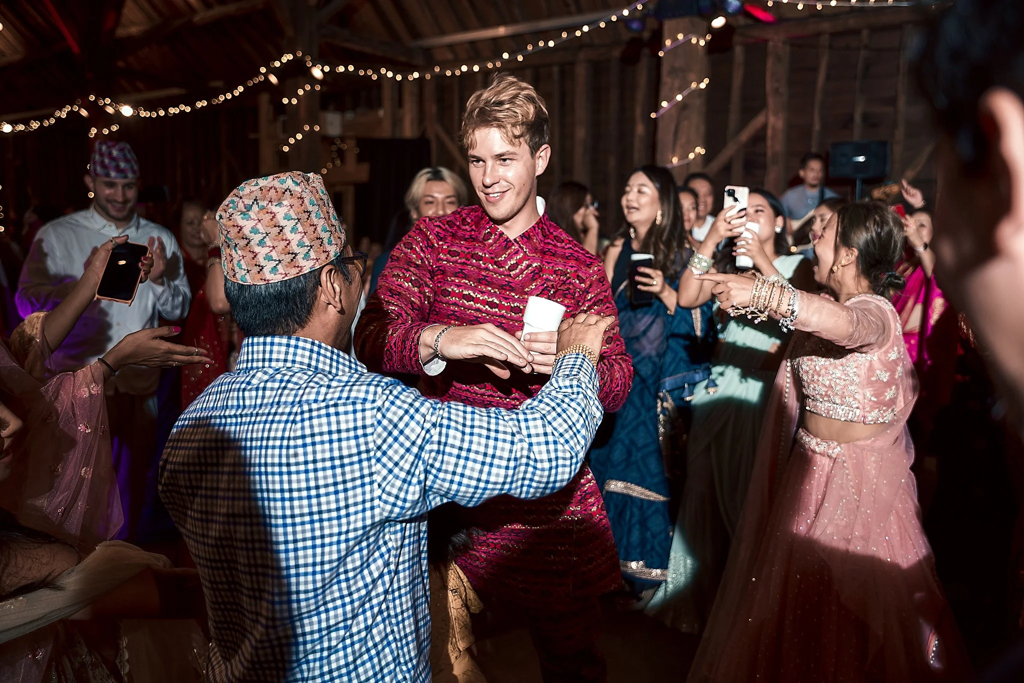 People celebrating and taking photos at a festive event with string lights, traditional attire, and joyful expressions.